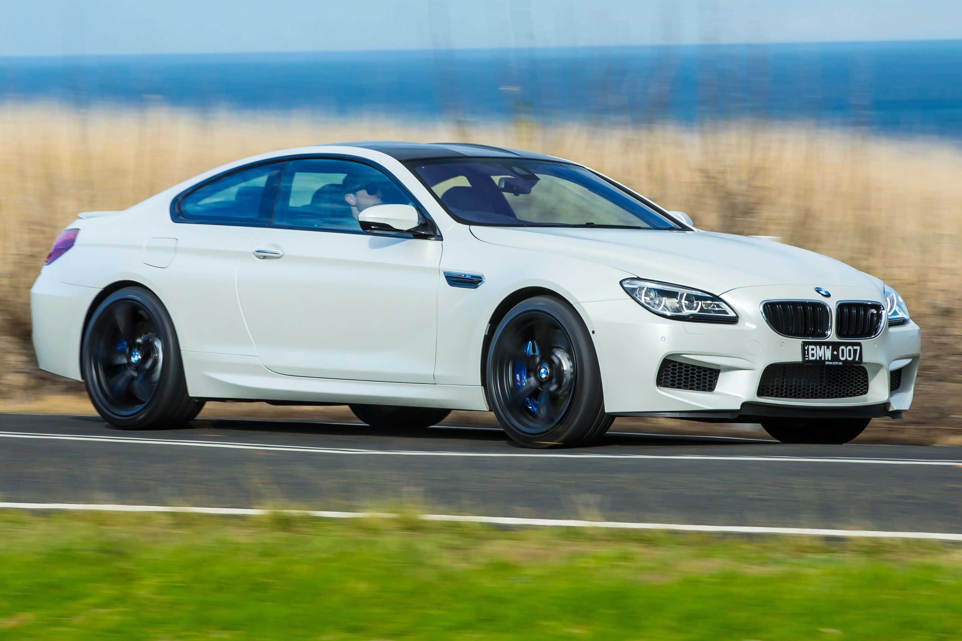 Bmw 6 Series 桌布 壁紙 — 一輛白色BMW M6雙門跑車沿著海岸公路飛馳，背景是模糊的草地和海洋。