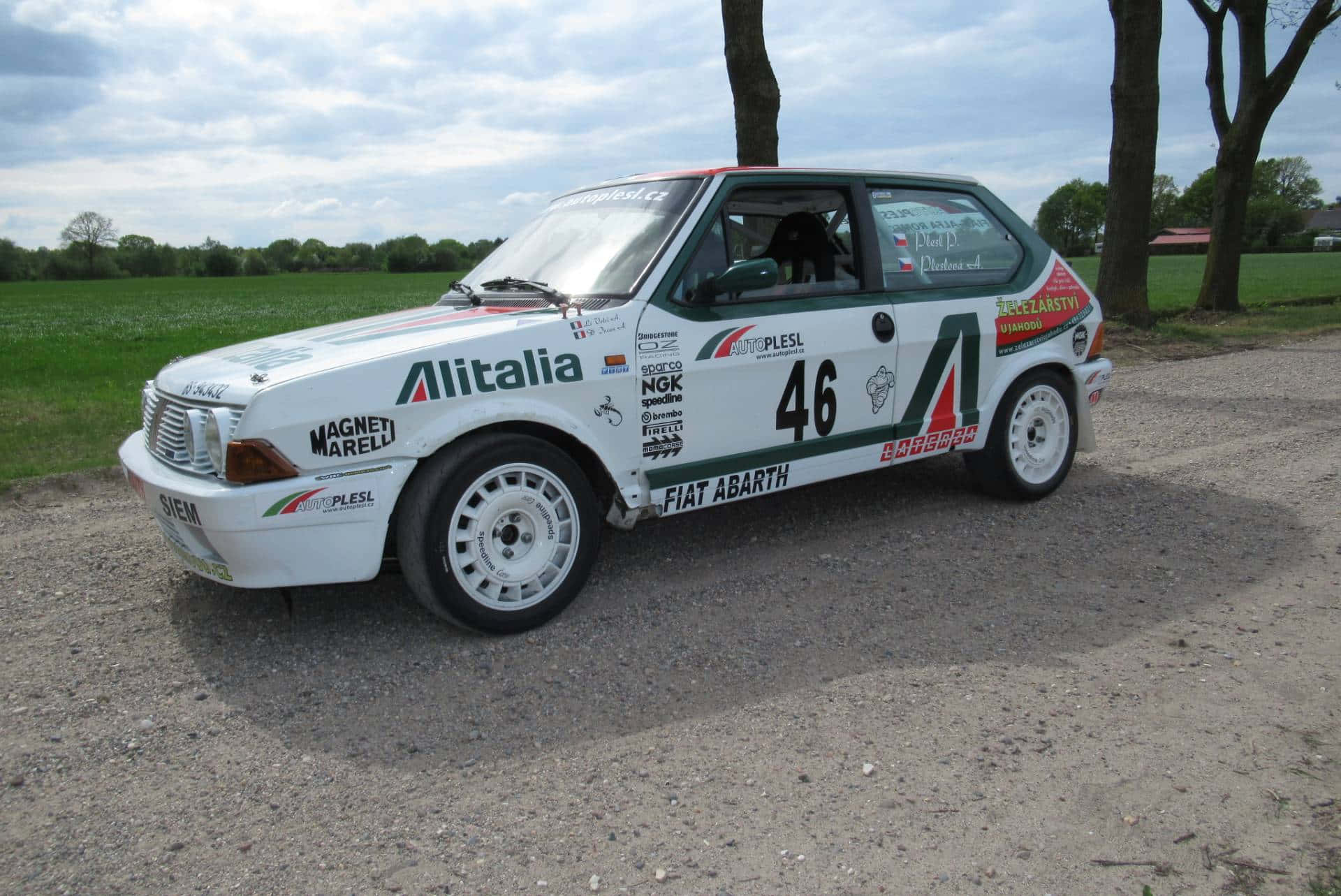 Fiat Ritmo 桌布 壁紙 — 一輛白色Fiat Abarth拉力賽車，編號46，停泊在碎石地上，旁邊有樹木，天空多雲。