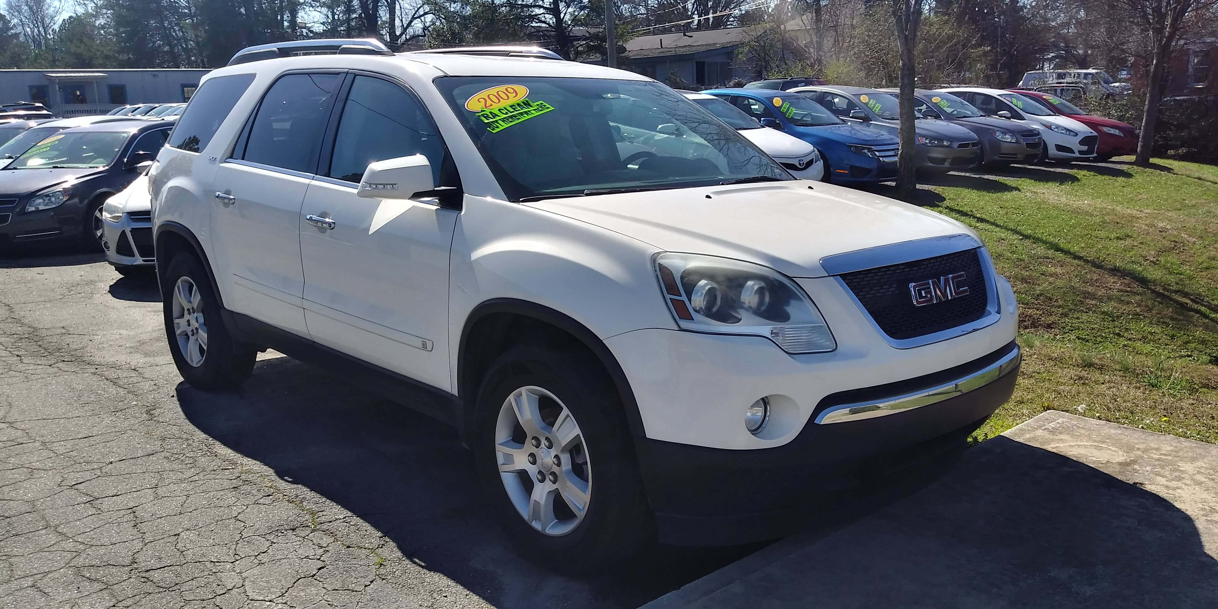 Gmc Acadia 桌布 壁紙 — 一輛白色GMC Acadia SUV停泊在陽光明媚的停車場，背景有其他汽車和樹木。