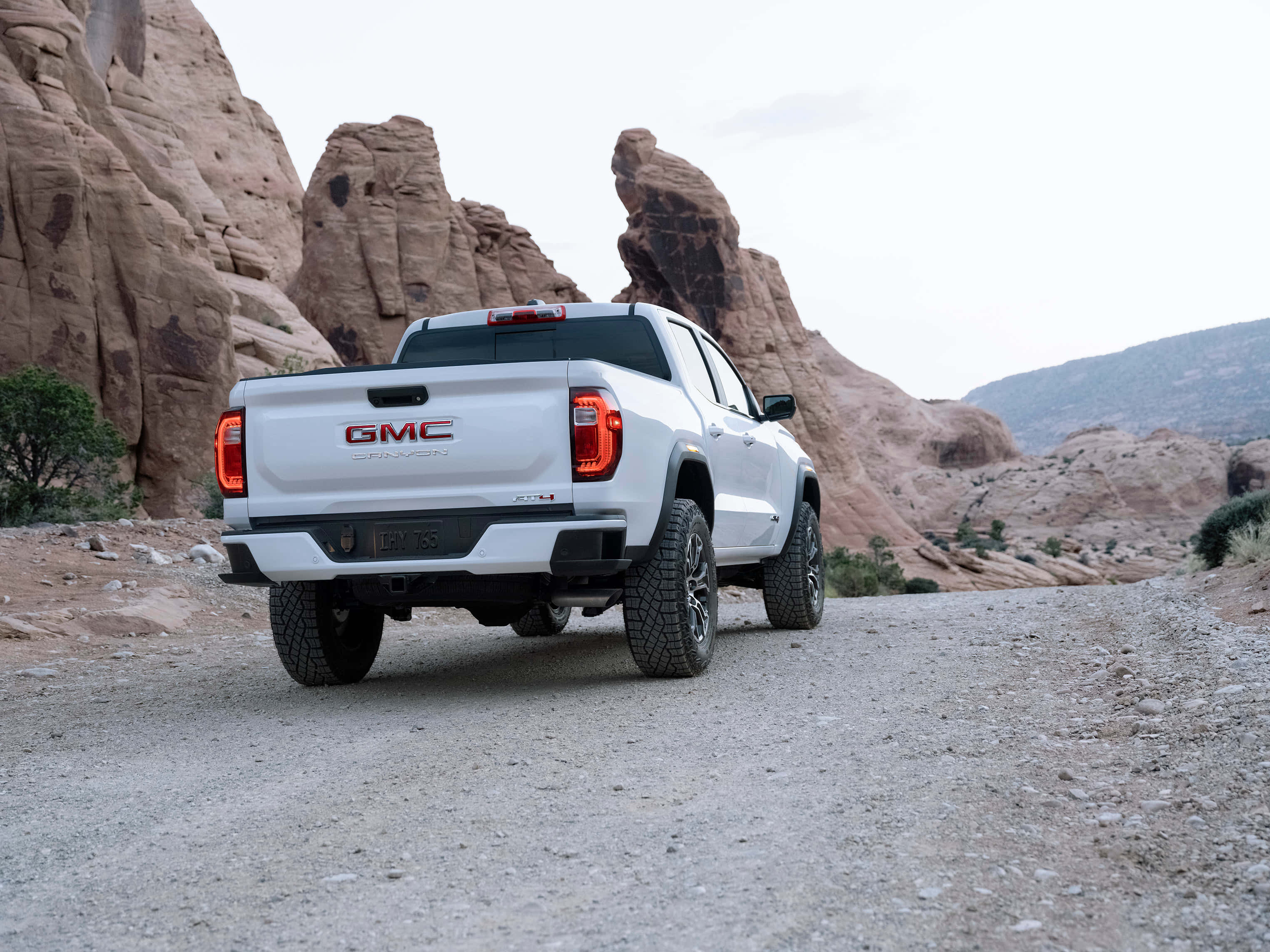 Gmc Canyon 桌布 壁紙 — 一輛白色GMC Sierra AT4 pickup truck在崎嶇的紅色岩石峽谷景觀中的碎石路上行駛。