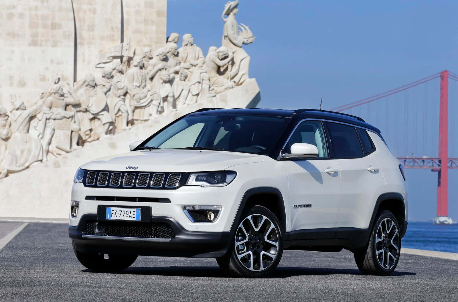 Family Car 桌布 壁紙 — 一輛白色Jeep Compass SUV停泊在發現者紀念碑前，背景是紅色的4月25日大橋，天空清澈湛藍。