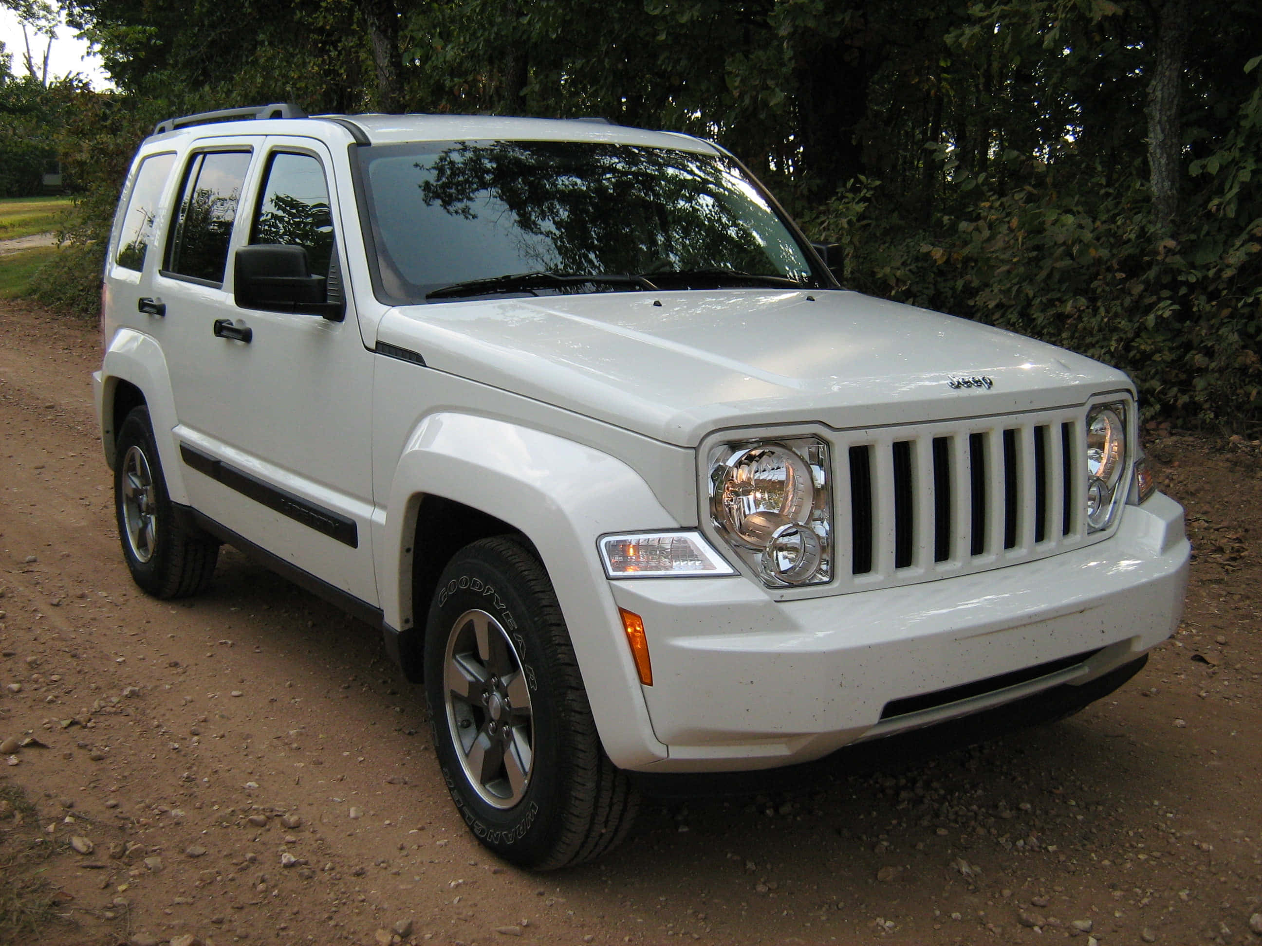 Jeep Liberty 桌布 壁紙 — 一輛白色Jeep Liberty SUV停泊在被茂密綠樹環繞的泥路上。
