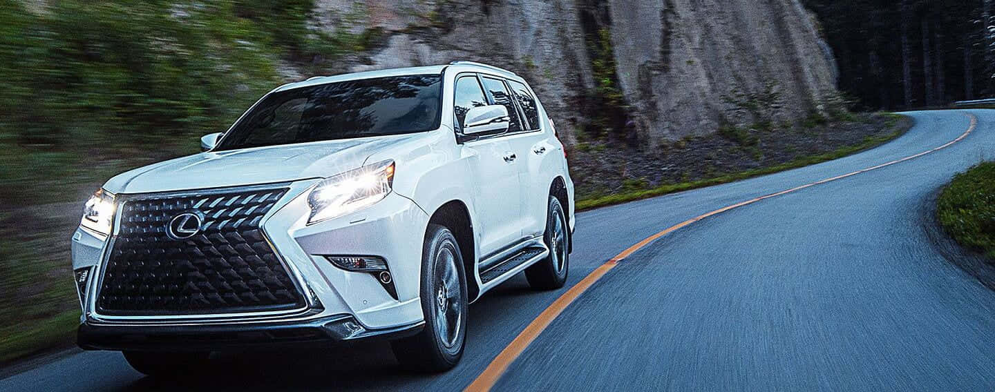 Lexus Gx 460 桌布 壁紙 — 一輛白色Lexus SUV沿著蜿蜒的山路疾馳，背景是模糊的綠樹和岩石峭壁。