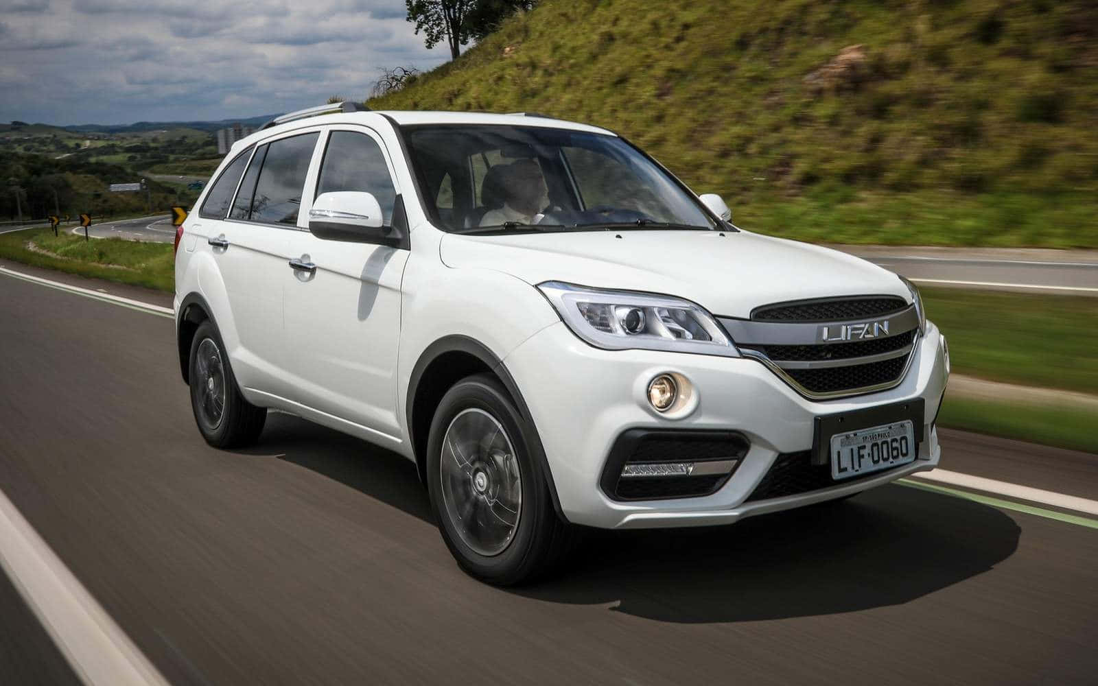 Lifan 桌布 壁紙 — 一輛白色Lifan SUV在蜿蜒的鄉村道路上疾馳，背景是綠色的山丘和多雲的天空。