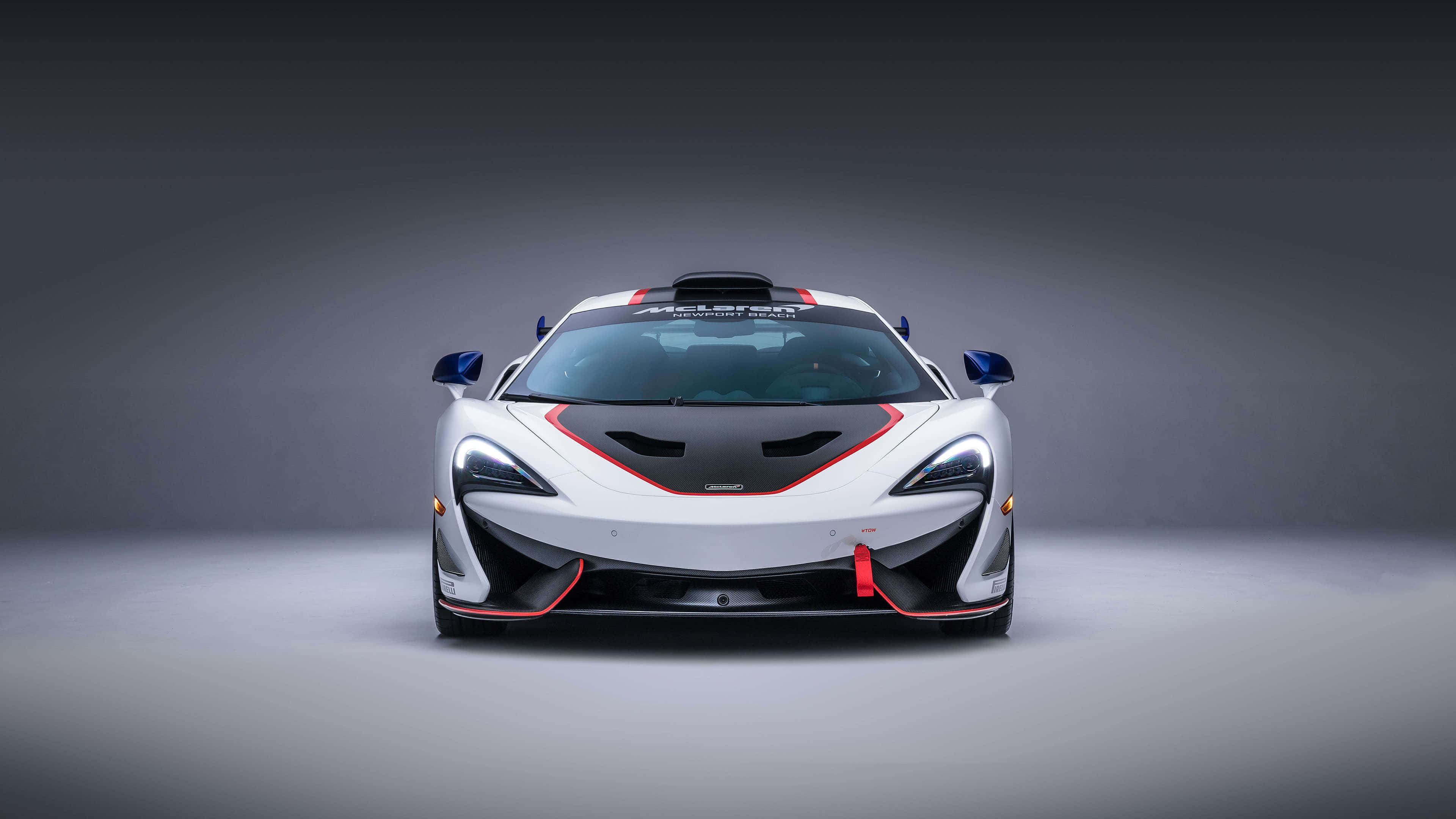 麥拿侖 桌布 壁紙 — 一輛白色McLaren賽車，帶有紅色和黑色點綴，在灰色背景下的工作室燈光下向前凝視。