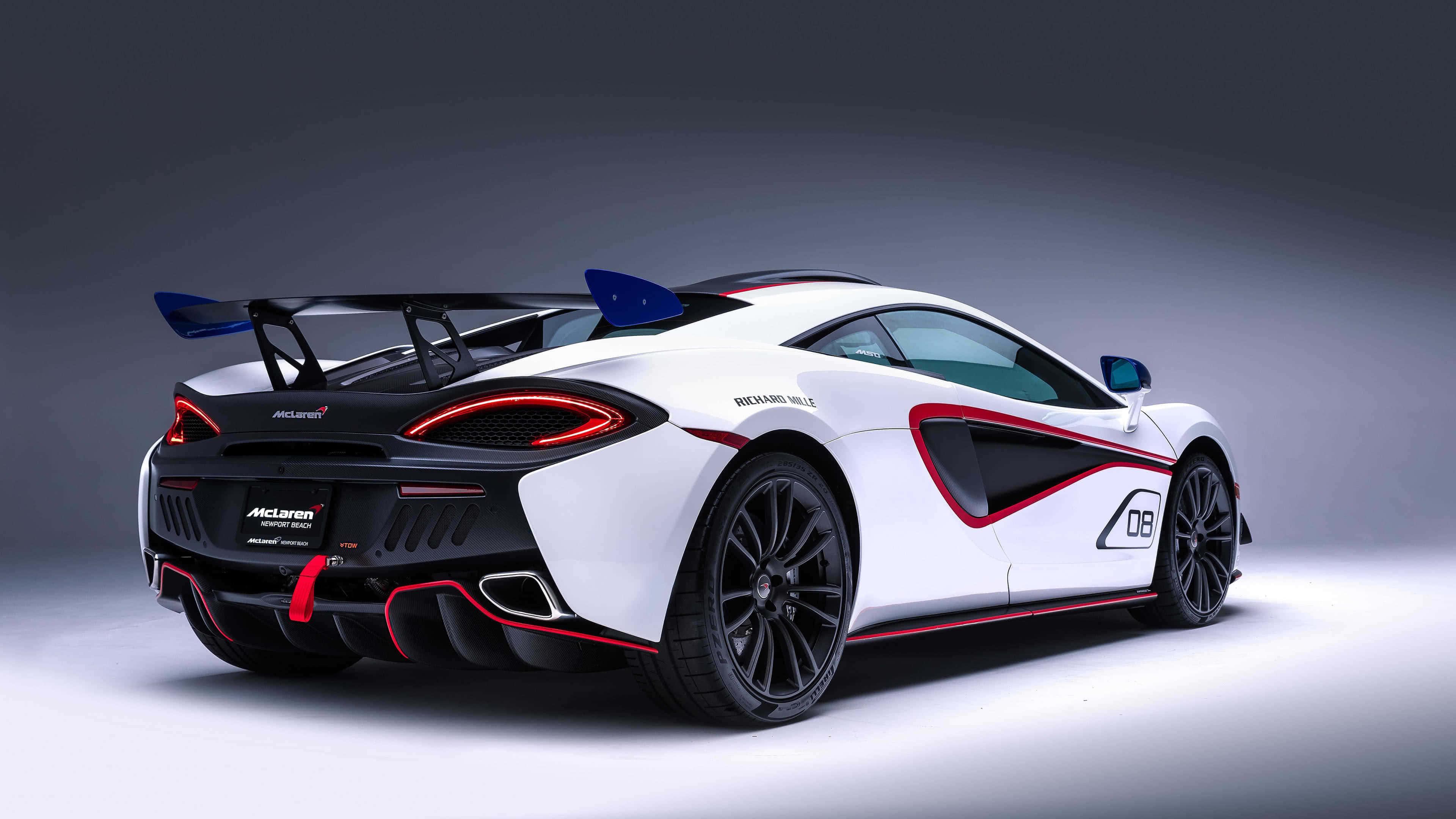麥拿侖 桌布 壁紙 — 一輛白色McLaren跑車帶有紅色點綴和大型尾翼，從後方四分之三角度展示，背景為深灰色工作室背景。