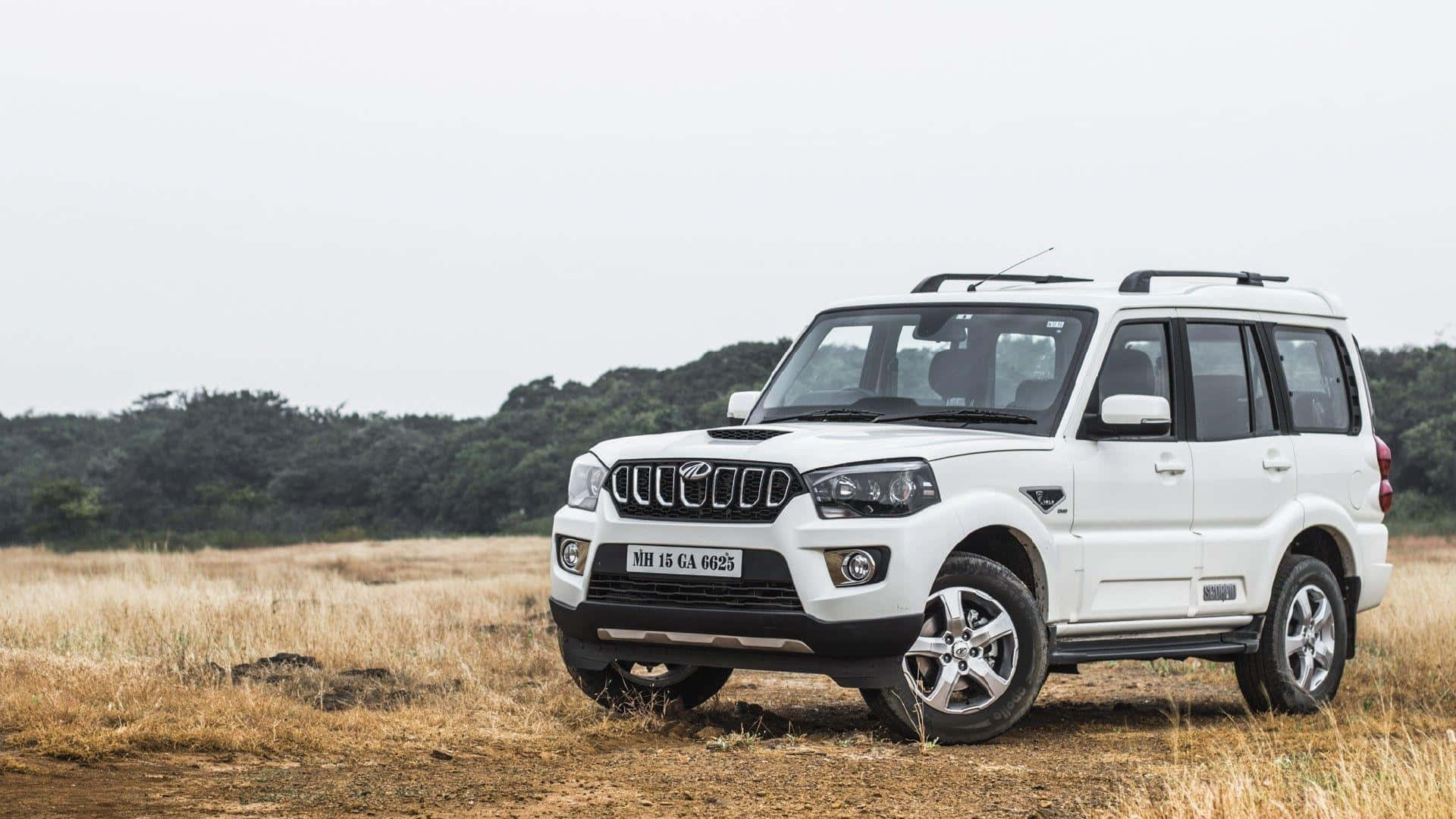 Mahindra 桌布 壁紙 — 一輛白色SUV停在一片乾燥的草地上，遠處有樹木，天空多雲。
