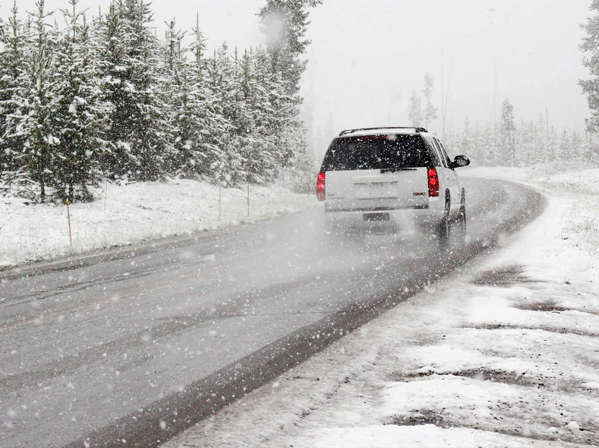 Winter Driving 桌布 壁紙 — 一輛白色SUV在強烈暴風雪中行駛在蜿蜒的森林道路上，兩旁是積雪的常青樹。