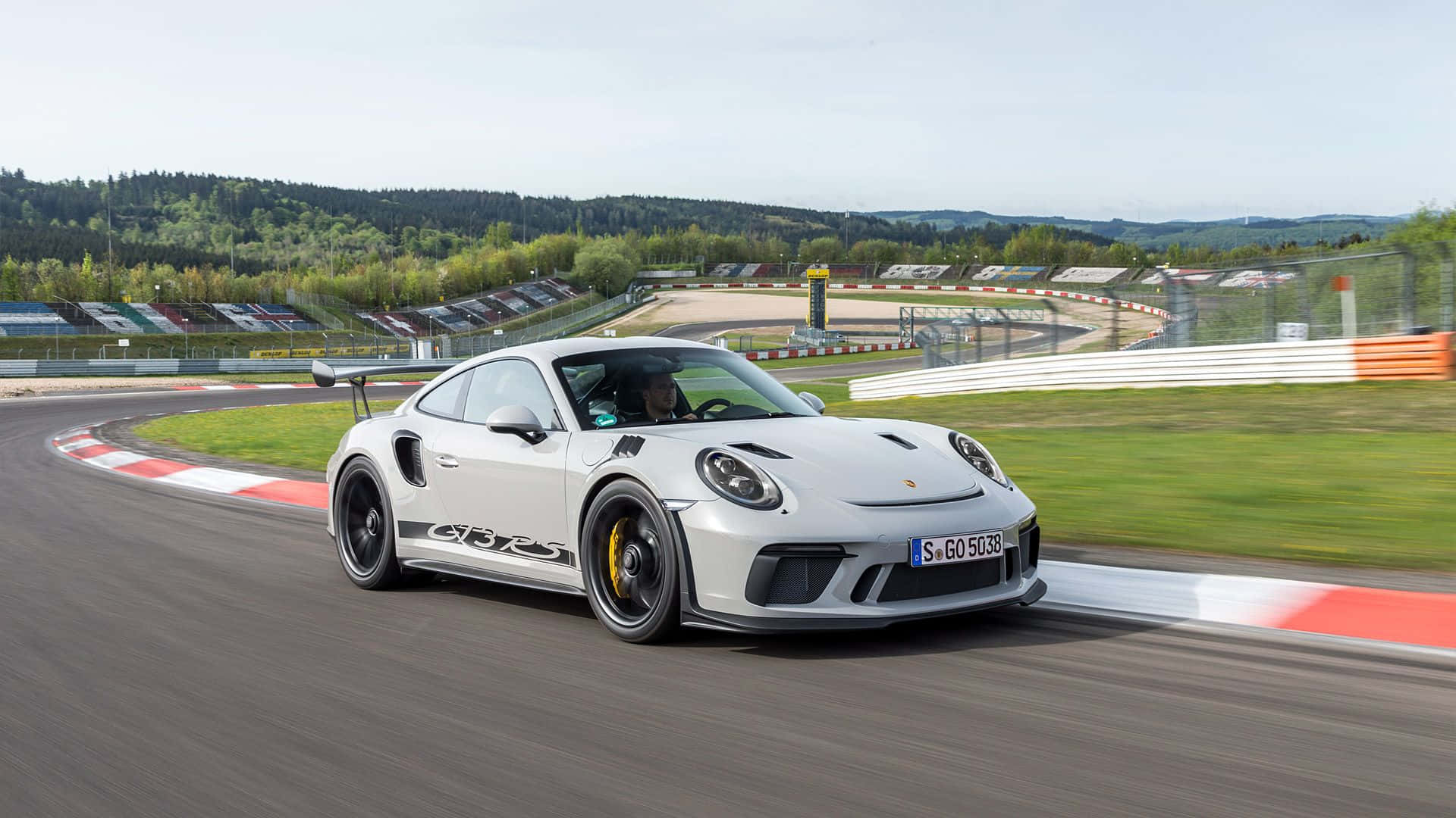 保時捷 桌布 壁紙 — 一輛白色保時捷911 GT2 RS在賽道彎位高速行駛，背景是模糊的綠色山丘和看台。