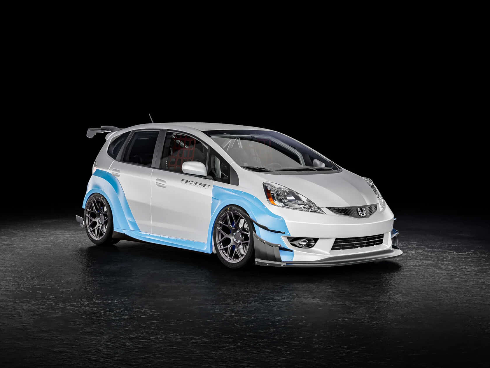 Honda Fit 桌布 壁紙 — 一輛白色和藍色改裝的本田Fit，配備黑色輪圈和賽車貼紙，在黑色背景的暗色攝影棚地板上蓄勢待發。