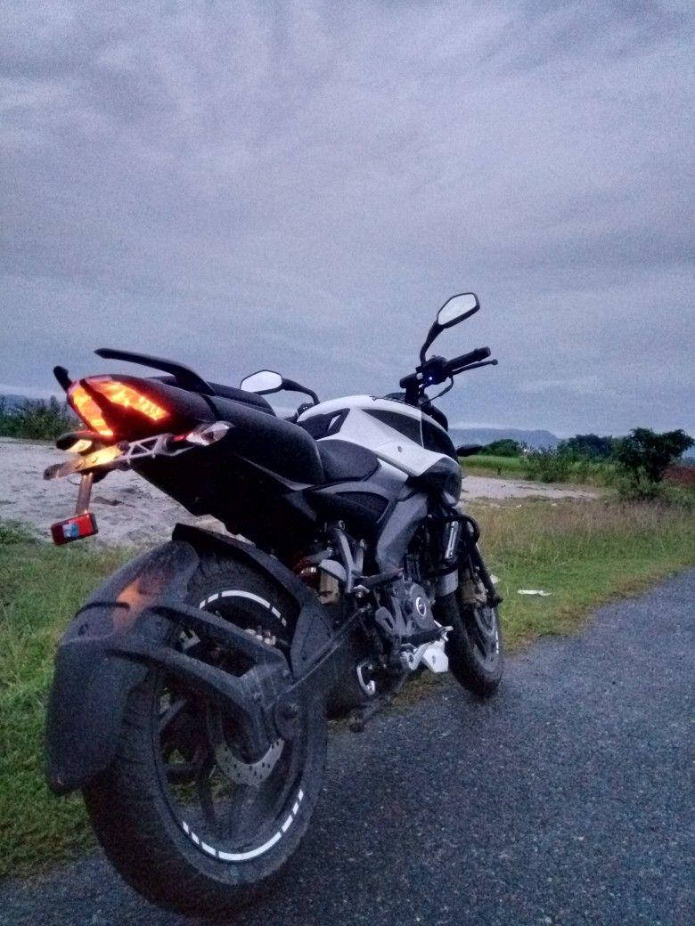 機車 桌布 壁紙 — 一輛白色和黑色的電單車，帶有發光的紅色尾燈，停泊在黃昏時分多雲天空下的碎石路上。