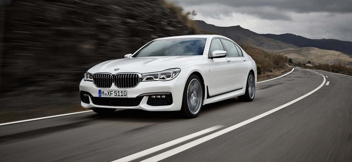 Bmw 7 Series 桌布 壁紙 — 一輛白色寶馬7系轎車在多雲的天空下沿著蜿蜒的山路疾馳。