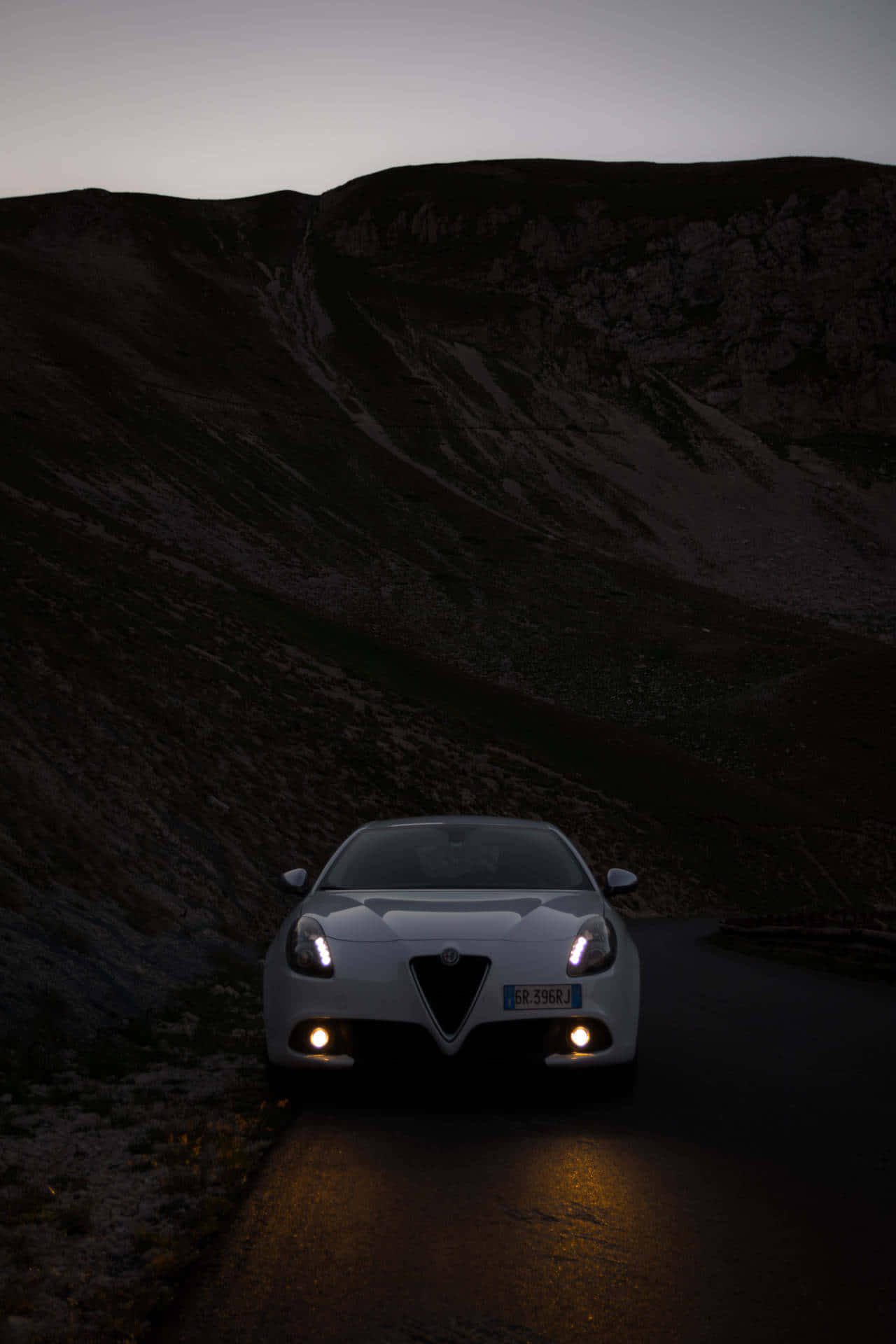 Alfa Romeo Giulietta 桌布 壁紙 — 一輛白色愛快羅密歐跑車的頭燈照亮了暮色中蜿蜒的山路。