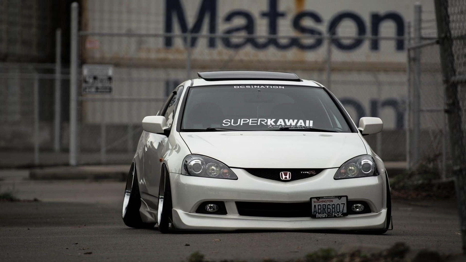 Rsx Type-s 桌布 壁紙 — 一輛白色改裝本田思域，帶有「SUPERKAWAII」貼紙，停在工業區靠近鐵絲網圍欄處。