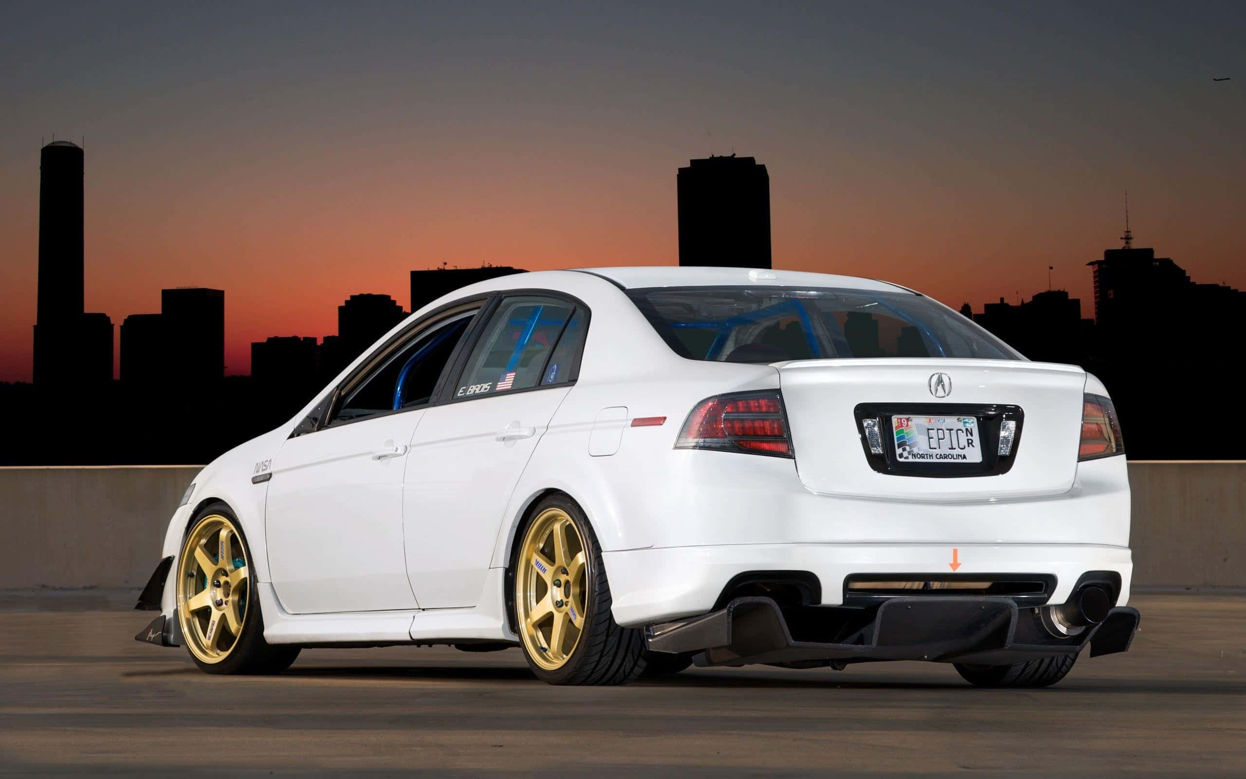 Rsx Type-s 桌布 壁紙 — 一輛白色改裝轎車配金色輪圈，停泊在日落時分的城市天橋上，背後是城市天際線的剪影。