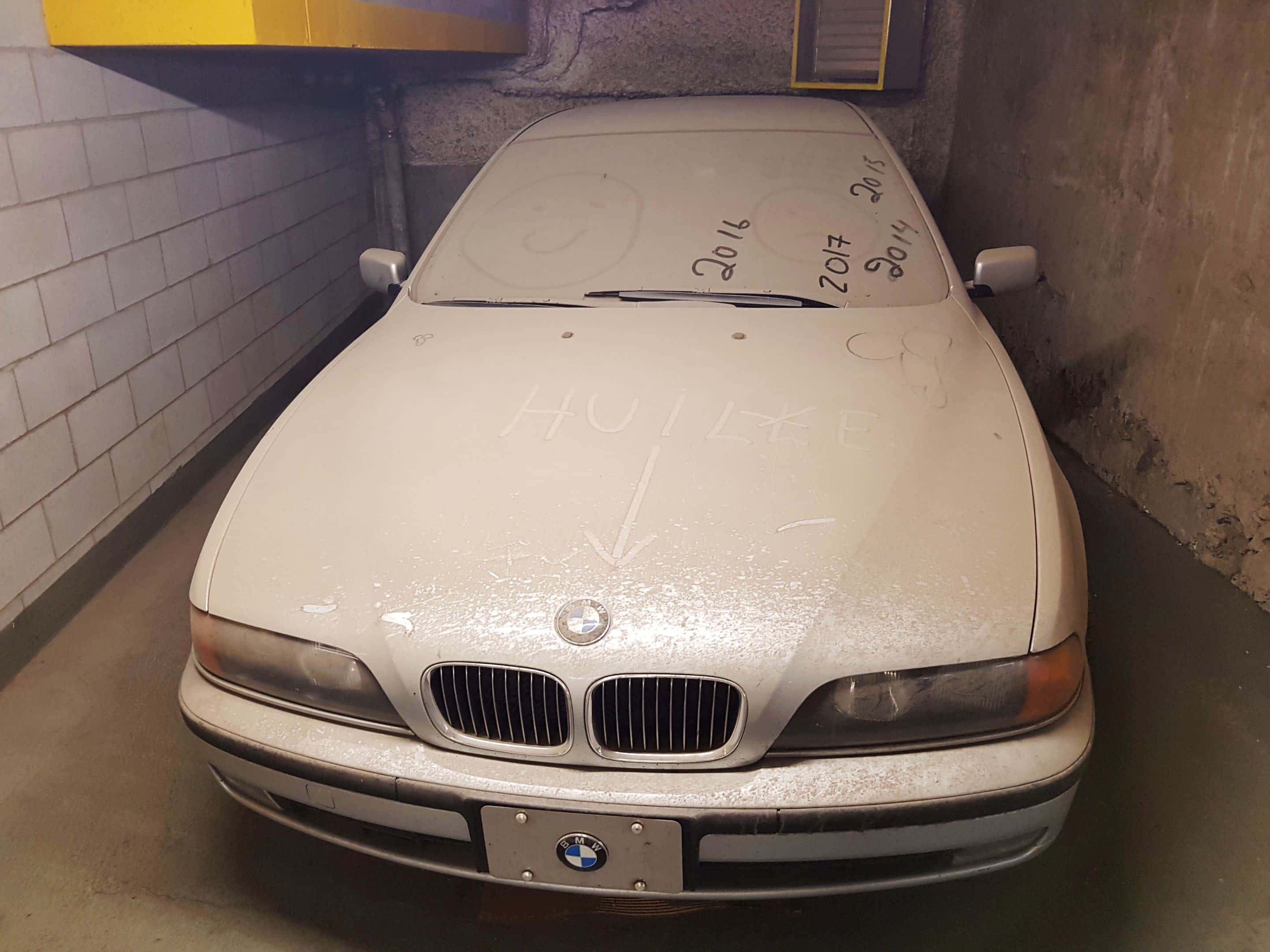 一輛白色汽車停在停車場 壁紙 — 一輛佈滿灰塵的白色BMW房車停放在昏暗的混凝土車庫中，引擎蓋上有塗鴉。