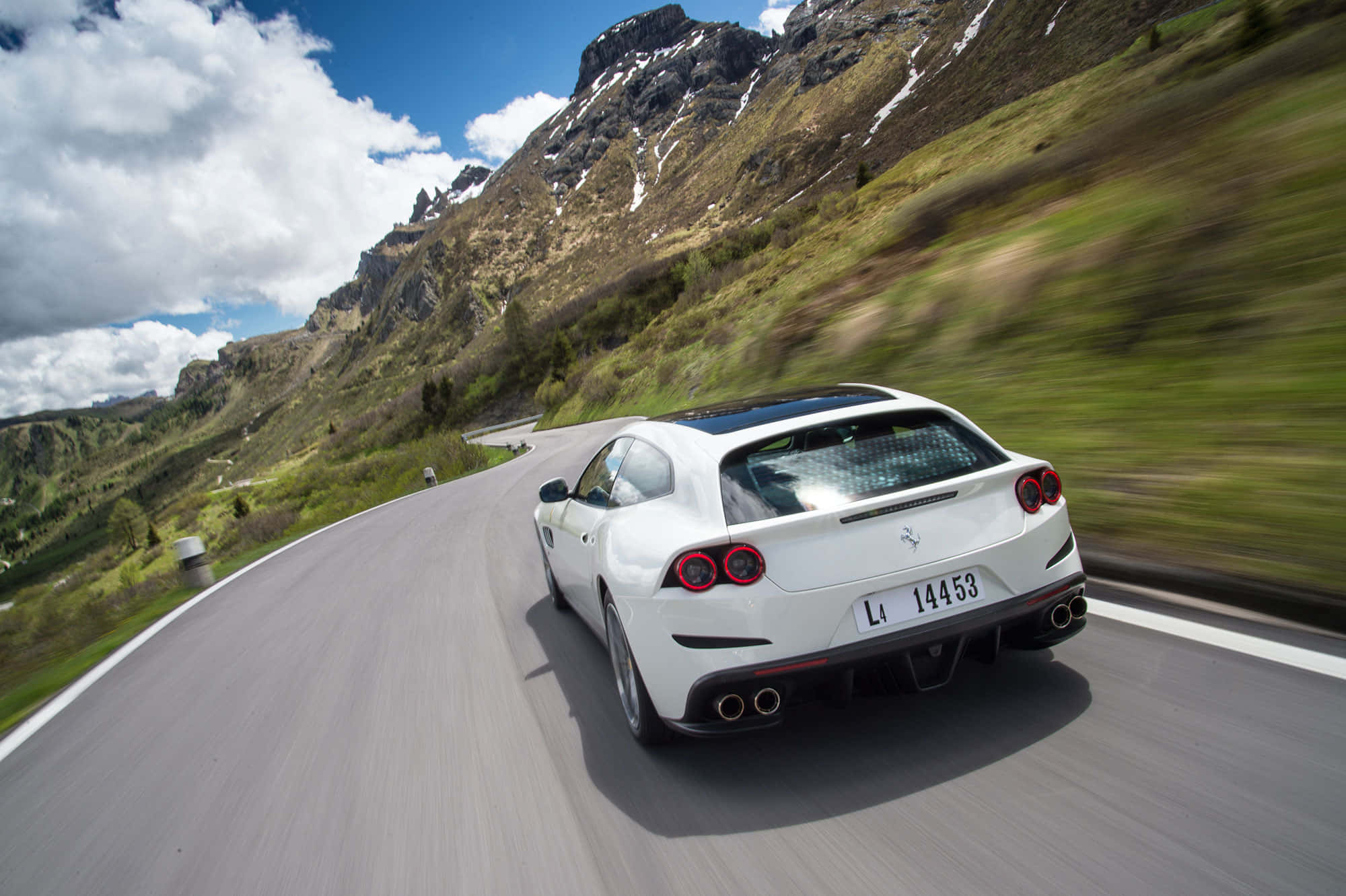 Ferrari Gtc4lusso 桌布 壁紙 — 一輛白色法拉利在蜿蜒的山路上飛馳，兩旁是白雪覆蓋的山峰和翠綠的山坡，頭頂是明亮的藍天。