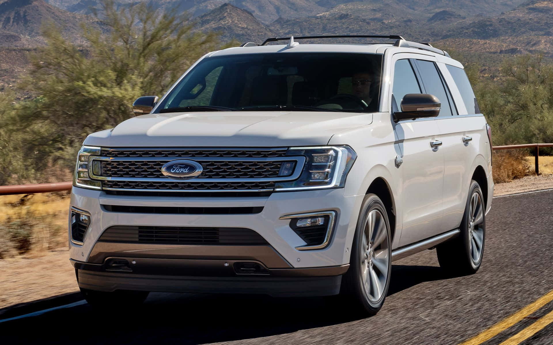 Ford Expedition 桌布 壁紙 — 一輛白色福特Expedition SUV在明亮的陽光下行駛在沙漠公路上，背景有山脈和灌木。