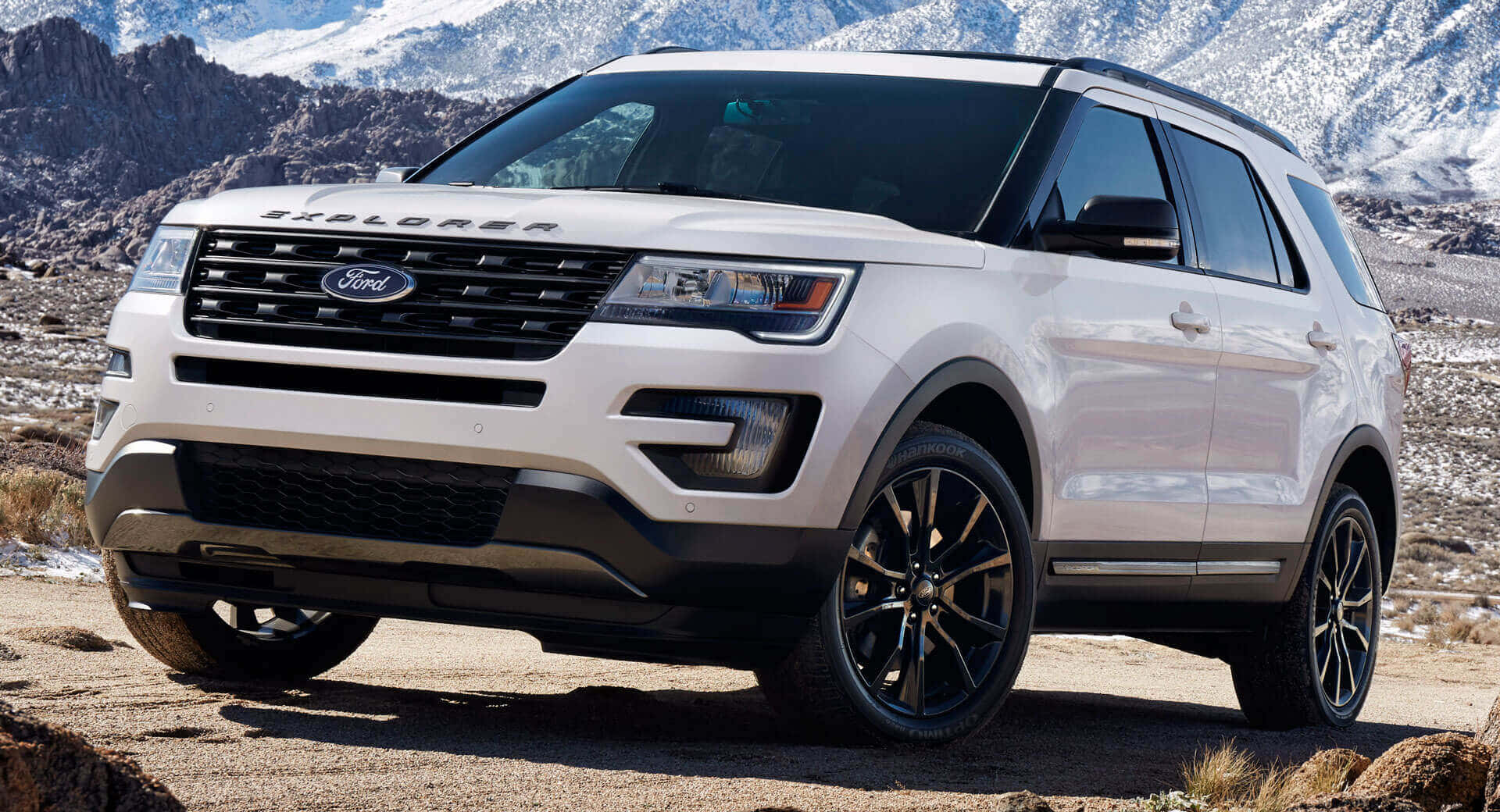 Ford Explorer 桌布 壁紙 — 一輛白色福特Explorer SUV停泊在岩石地形上，背景是白雪覆蓋的山脈，在明亮的日光下。