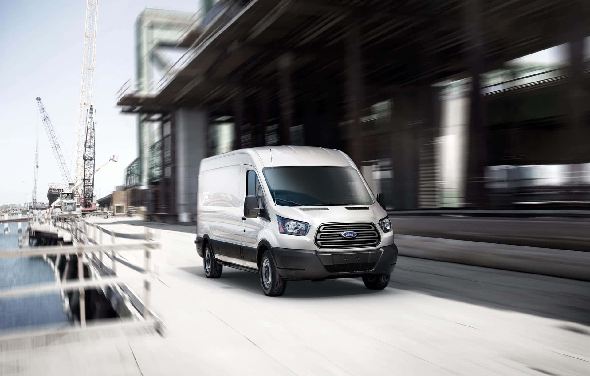 Ford Transit 桌布 壁紙 — 一輛白色福特全順客貨車沿著現代化海濱道路疾馳，在工業建築和起重機周圍產生動態模糊效果。