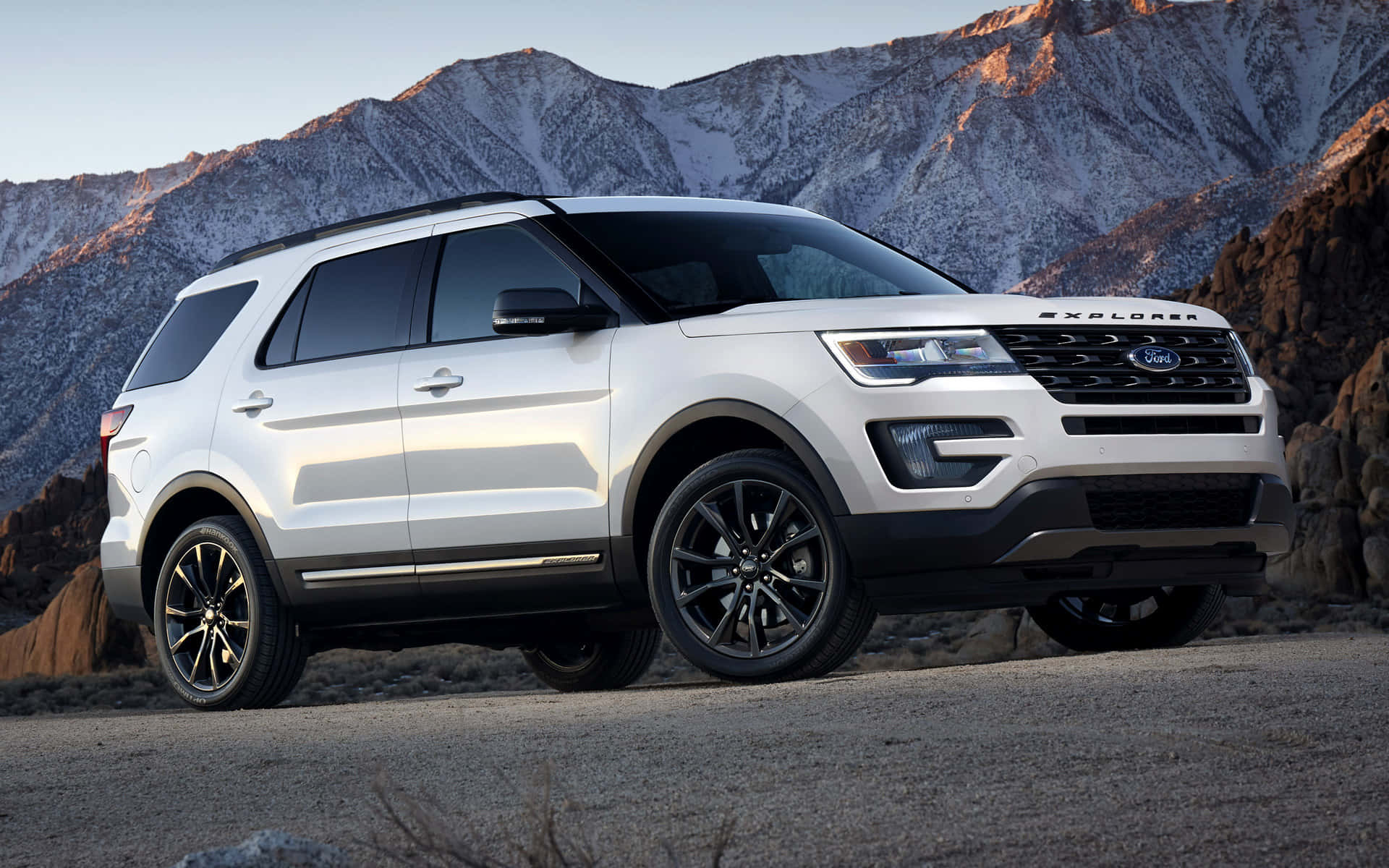 Ford Explorer 桌布 壁紙 — 一輛白色福特探險者SUV在日出時停泊在碎石路上，背景是積雪的山峰。