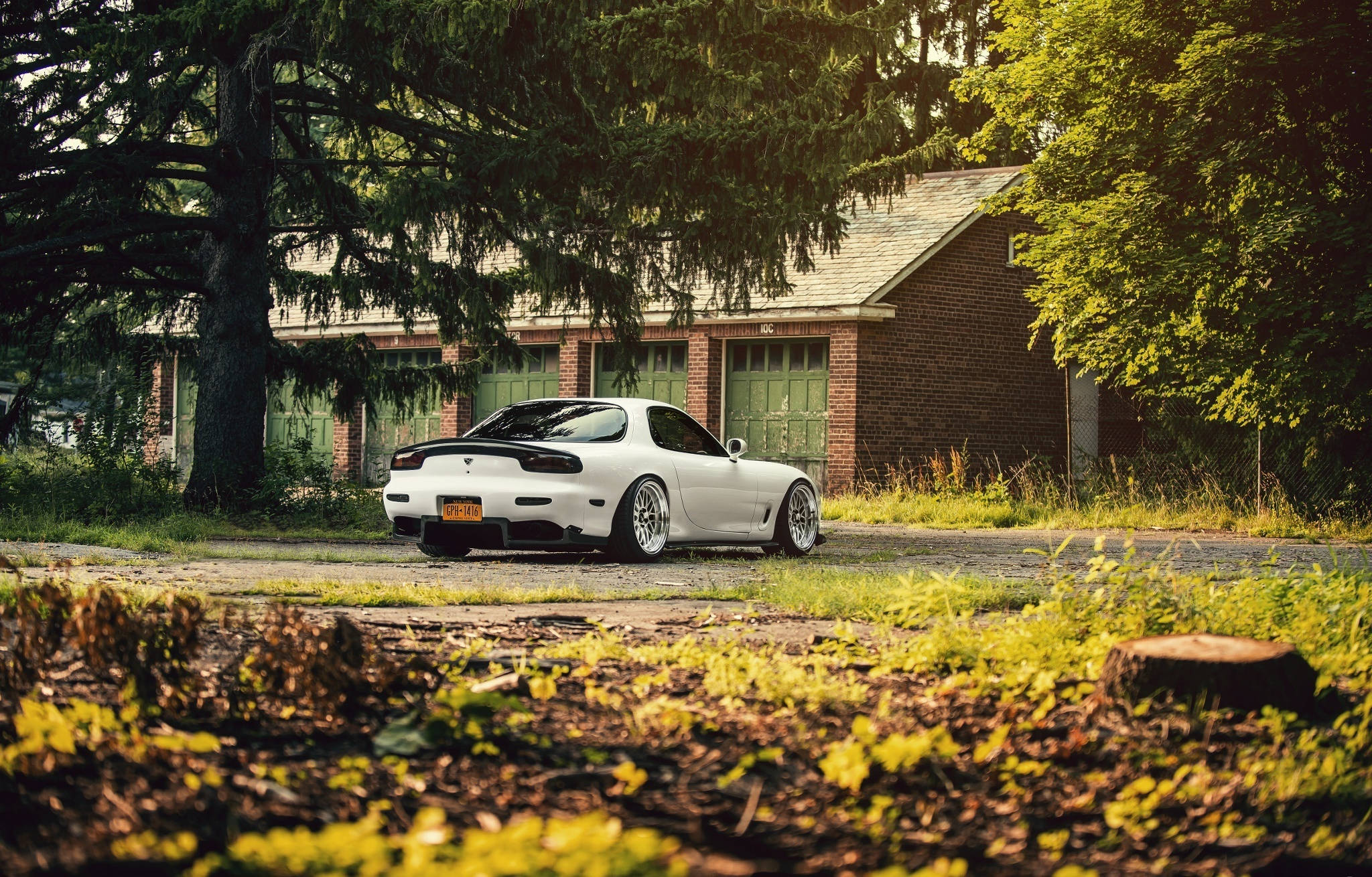 Mazda 桌布 壁紙 — 一輛白色萬事得RX-7跑車停泊在磚屋前的碎石車道上，周圍環繞著茂密的綠樹。