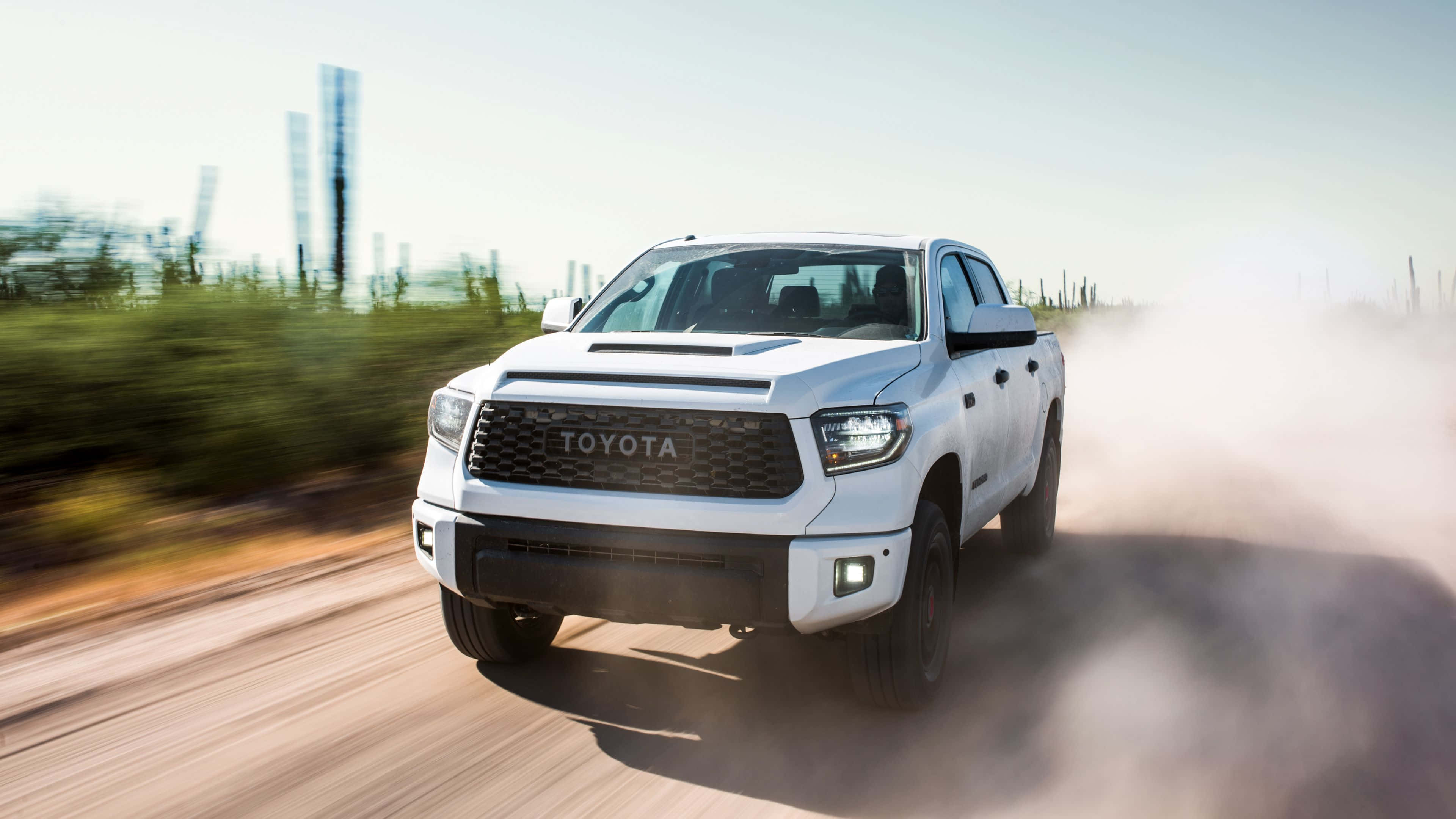 Toyota 桌布 壁紙 — 一輛白色豐田皮卡在明亮的日光下，在塵土飛揚的鄉村道路上高速行駛，揚起滾滾塵土。