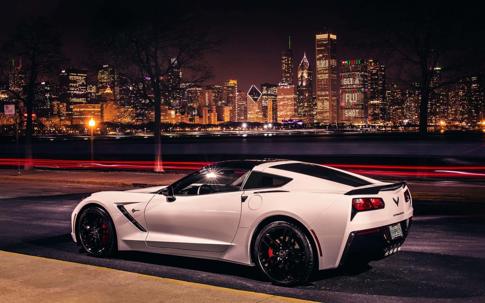 Chevrolet Corvette Stingray 桌布 壁紙 — 一輛白色跑車在夜間停泊，背後是充滿活力的城市天際線閃耀著光芒。