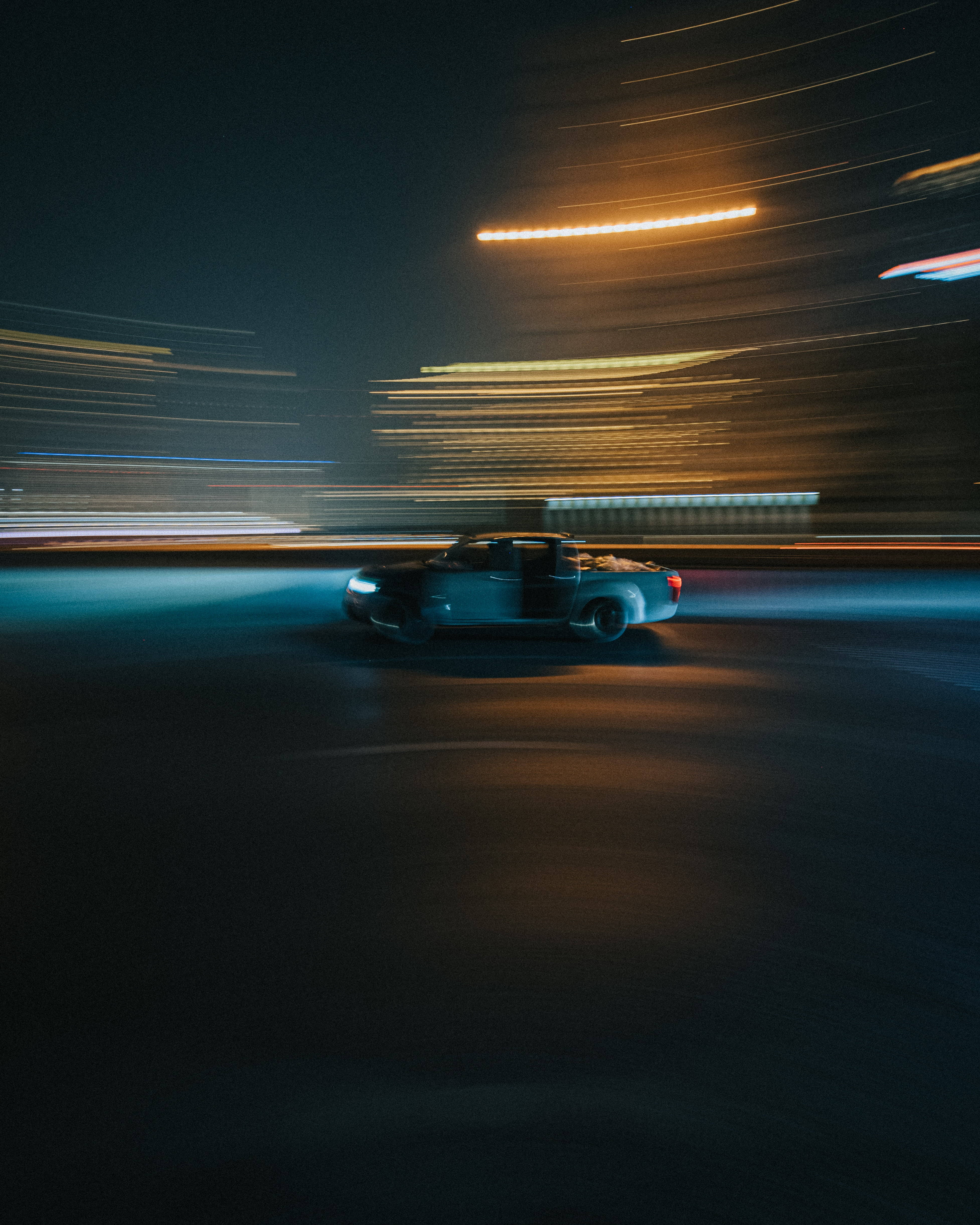 driving fast 桌布 壁紙 — 一輛皮卡車在夜晚霓虹燈閃爍的城市中疾馳，留下光跡。