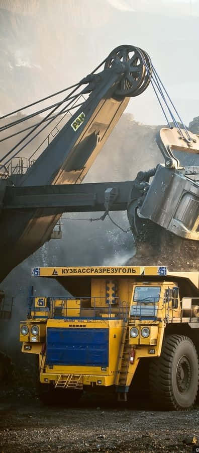 一輛空載的黃色自卸車駛在路上 壁紙 — 一架巨大的黃色礦用自卸車在明亮的日光下，於塵土飛揚的露天礦場中從巨型挖掘機接收煤炭。