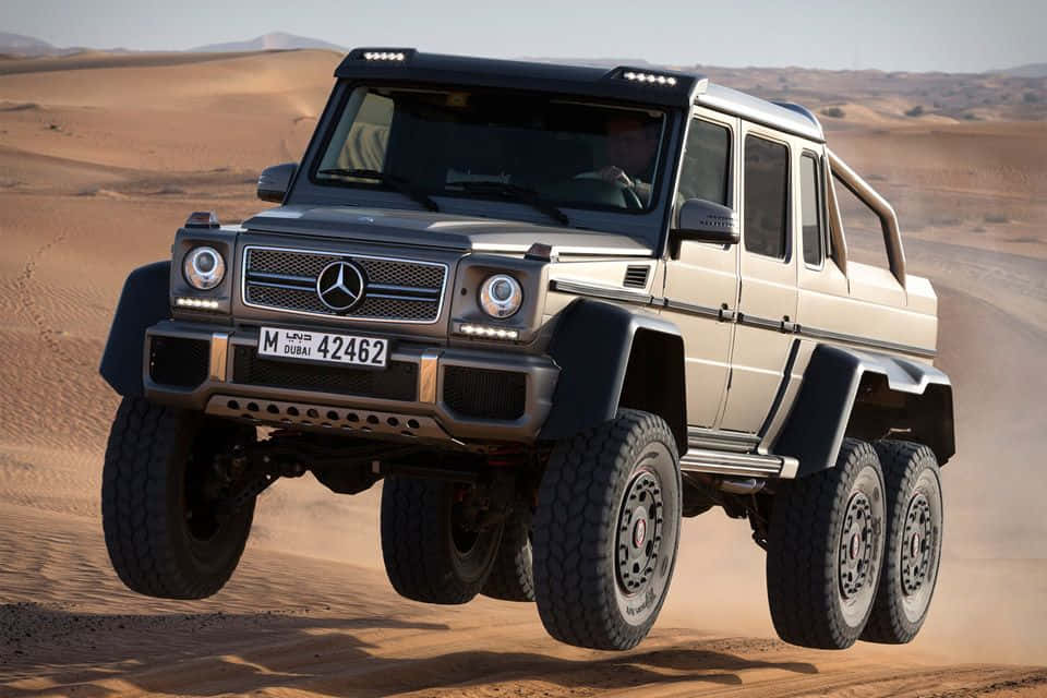 Off-road Car 桌布 壁紙 — 一輛米色 Mercedes-Benz G63 AMG 6x6 越野卡車飛躍金色沙漠沙丘，塵土飛揚。
