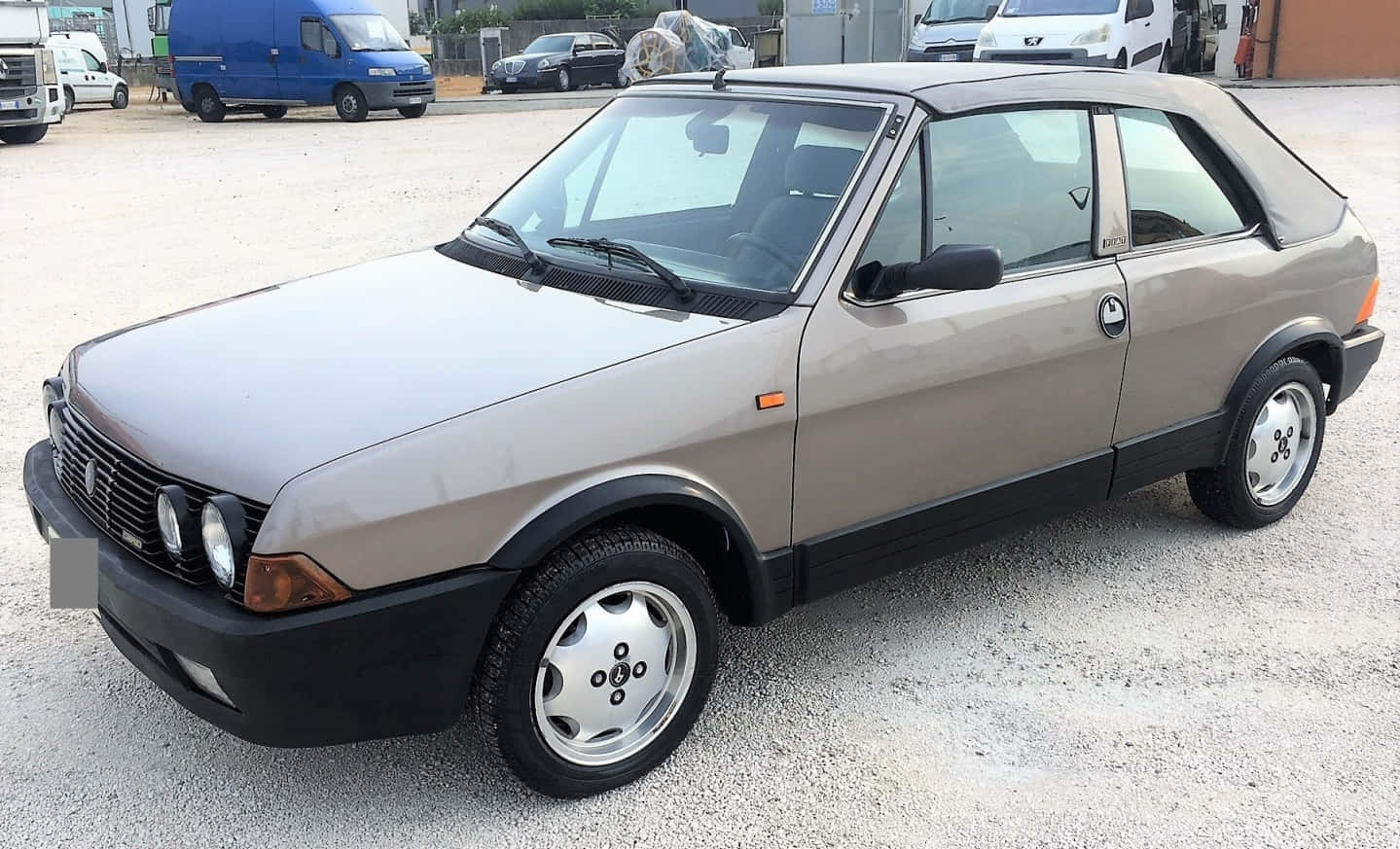 Fiat Ritmo 桌布 壁紙 — 一輛米色Fiat Uno Turbo掀背車停在碎石地上，背景有其他車輛。