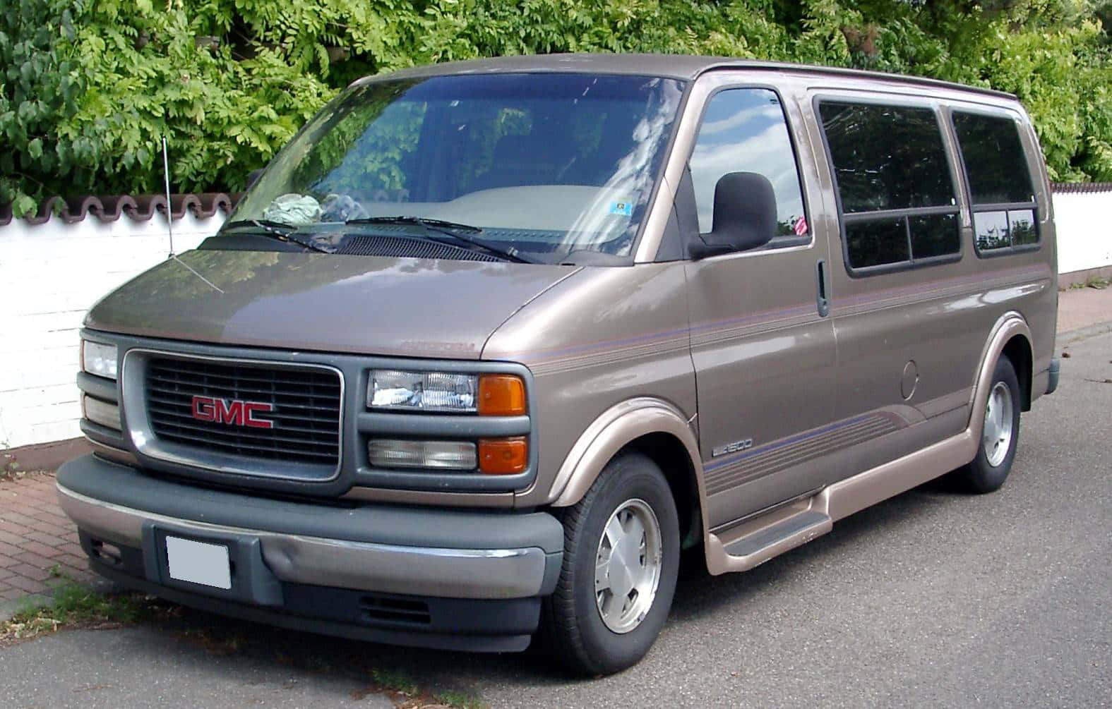 Gmc Savana 桌布 壁紙 — 一輛米色GMC Safari小型貨車停泊在鋪砌的車道上，旁邊有白色圍欄和茂密的綠色樹葉。