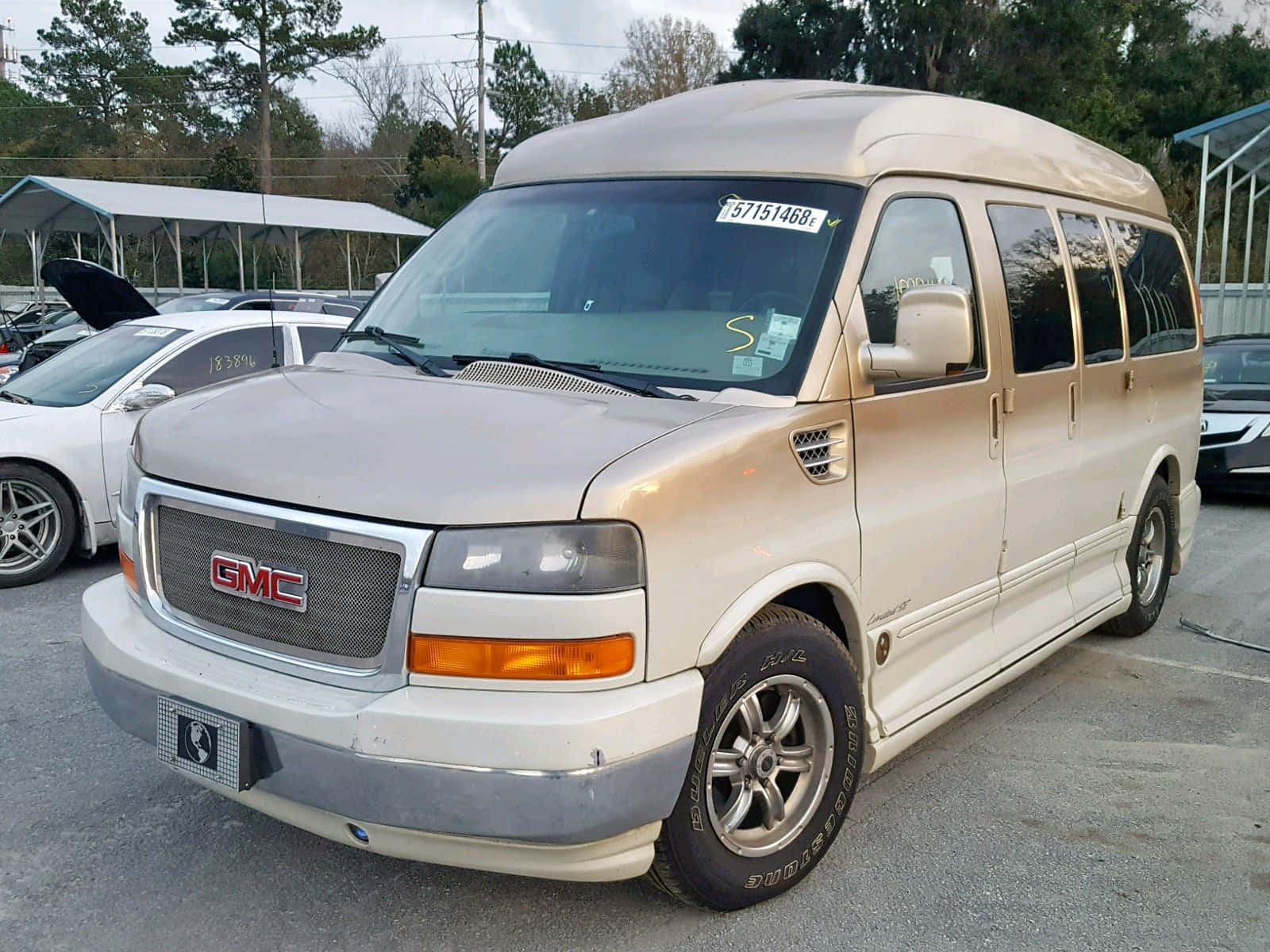 Gmc Savana 桌布 壁紙 — 一輛米色GMC露營車停泊在停車場，背景有樹木和其他車輛。