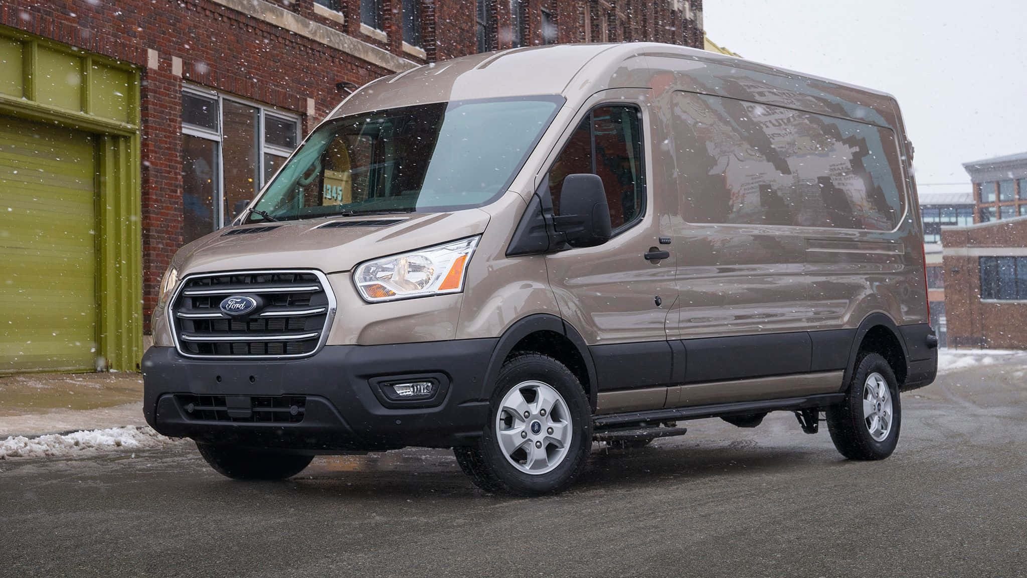 Ford Transit 桌布 壁紙 — 一輛米色福特 Transit 客貨車停在磚砌建築外，周圍輕輕飄落著雪花。