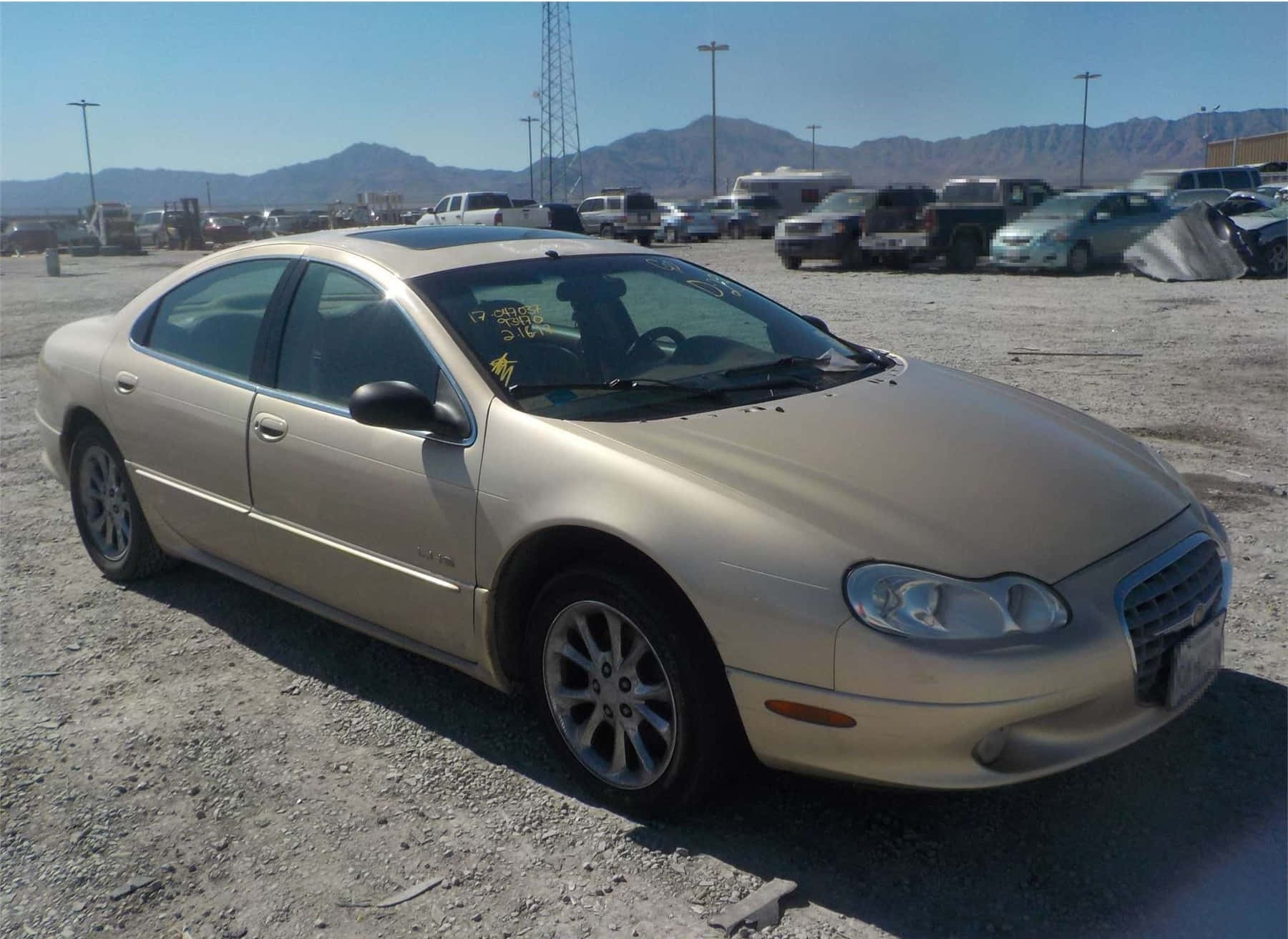 Chrysler Lhs 桌布 壁紙 — 一輛米色轎車停泊在陽光明媚的碎石地上，背景有山巒。