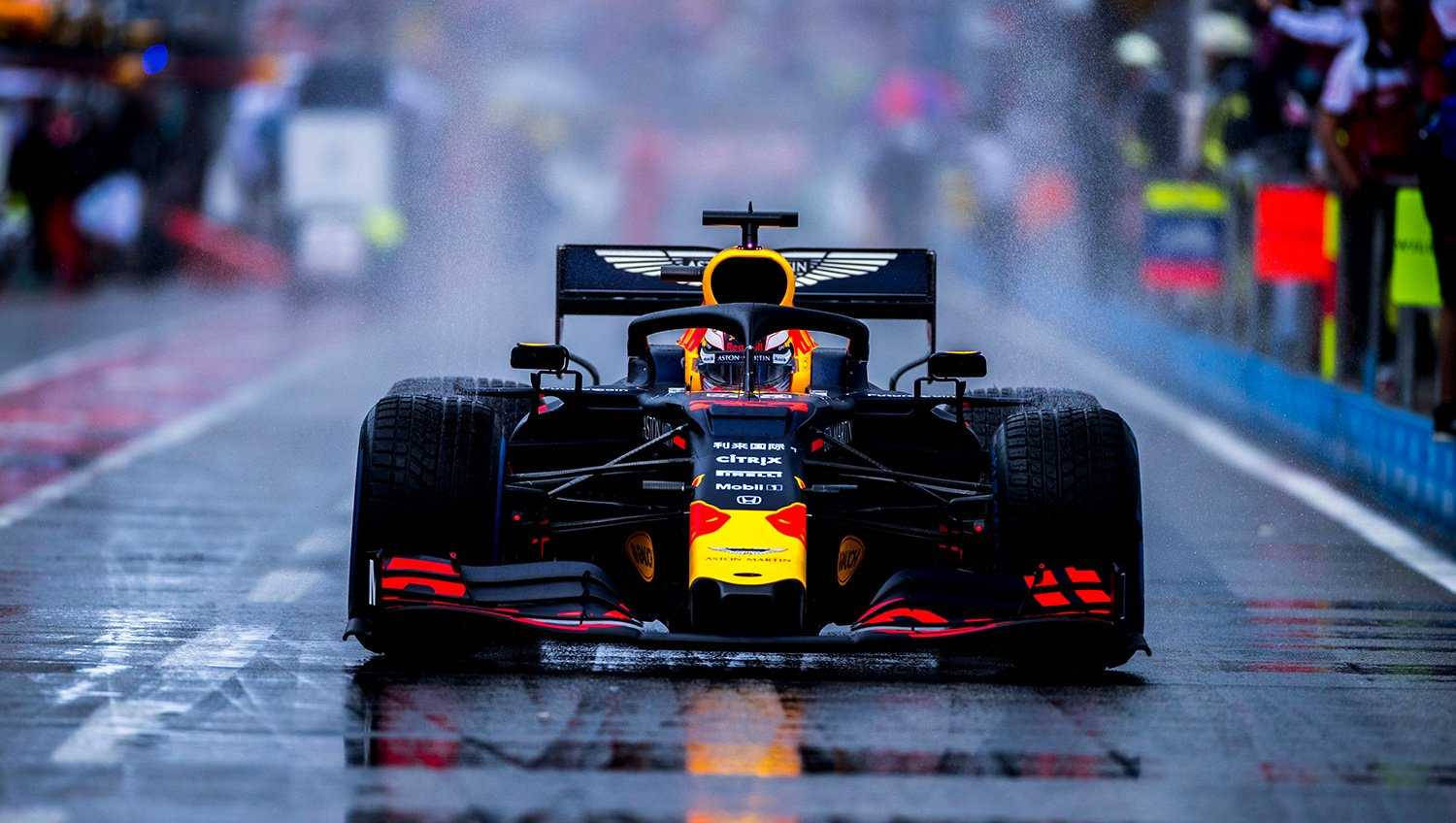 Verstappen 桌布 壁紙 — 一輛紅牛一級方程式賽車在濕滑的賽道上疾馳，濺起水花，觀眾從模糊的邊線觀看。