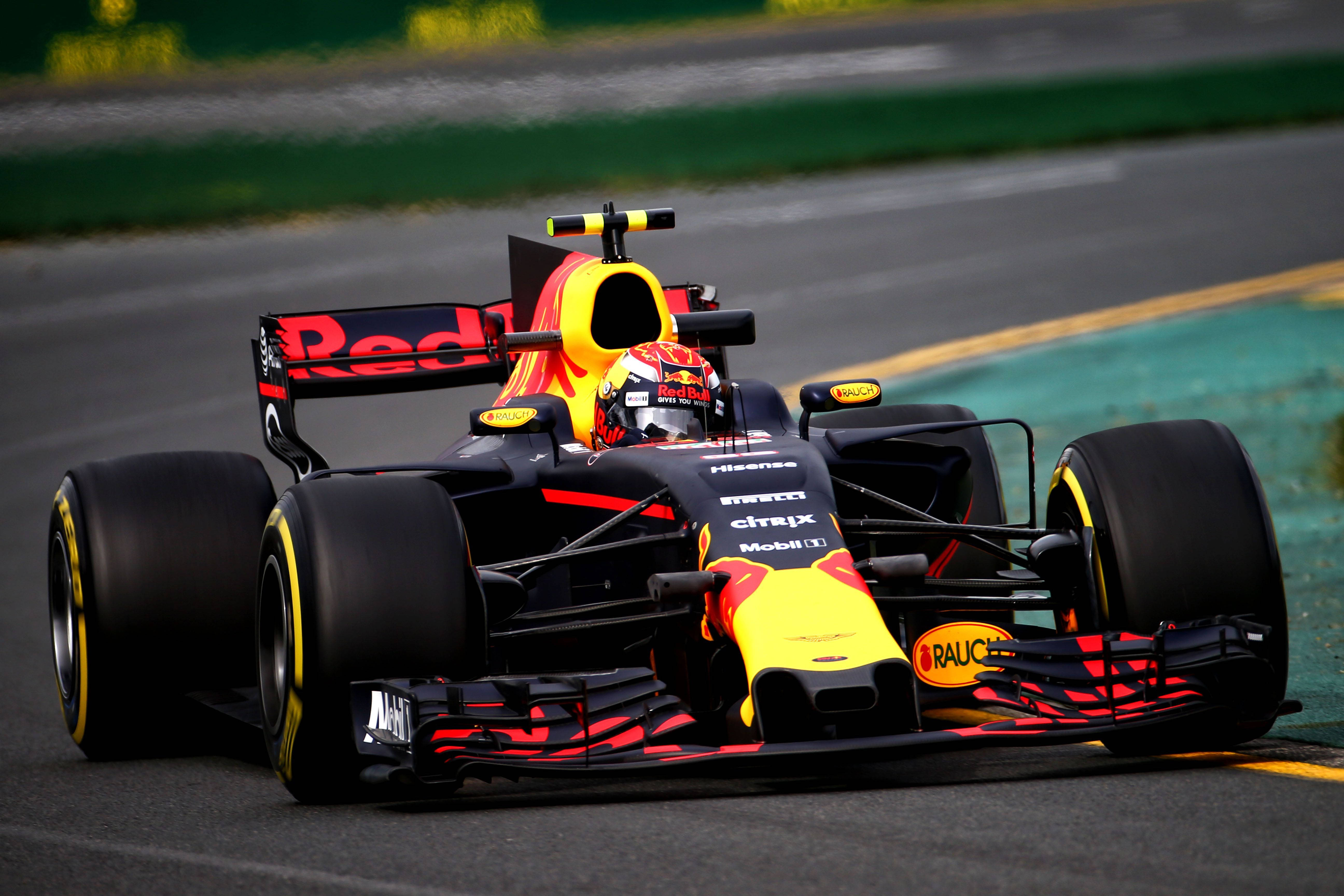 Verstappen 桌布 壁紙 — 一輛紅牛一級方程式賽車在賽道上疾馳，帶有鮮豔的黃色和紅色點綴，背景是模糊的綠色和灰色。