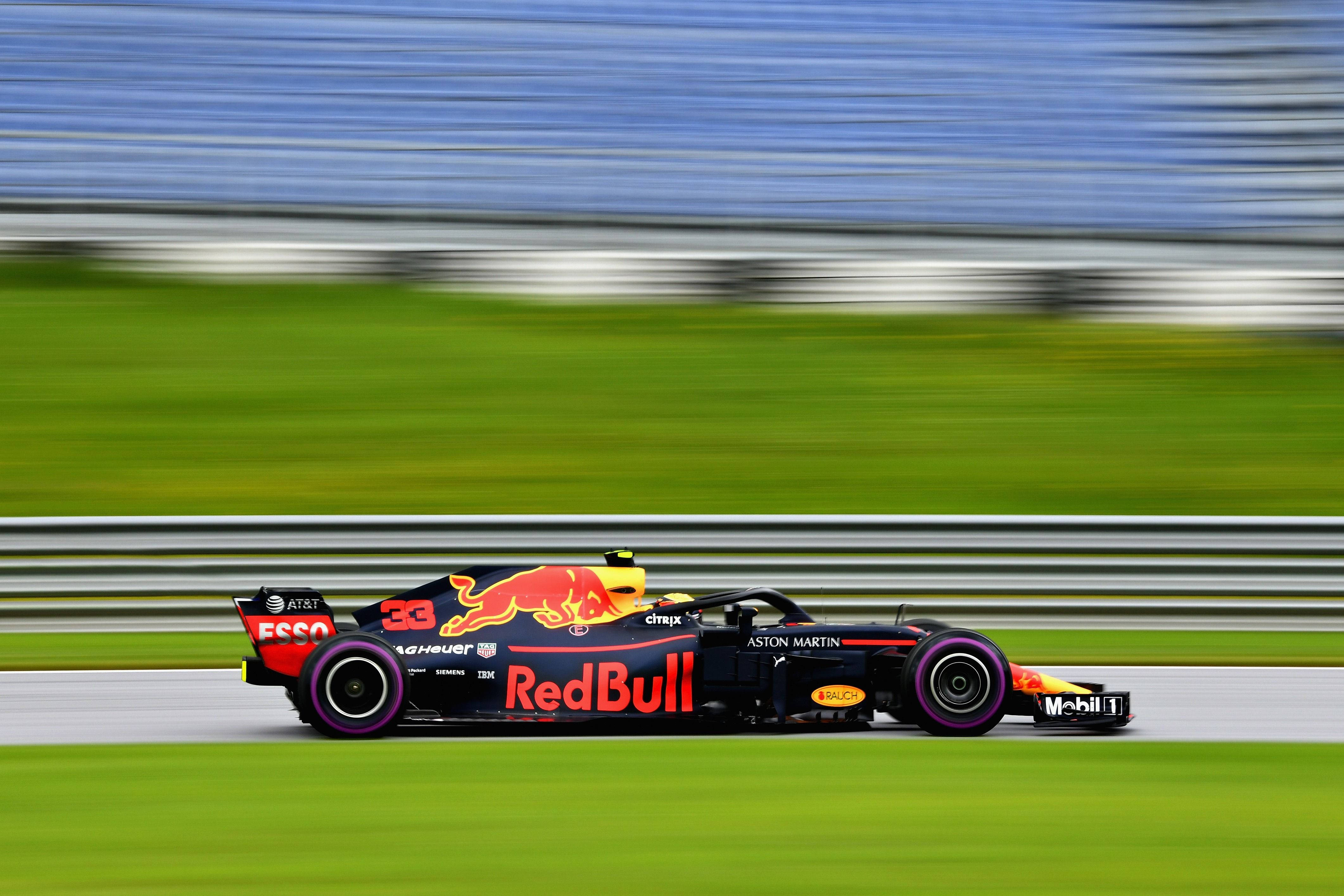Verstappen 桌布 壁紙 — 一輛紅牛一級方程式賽車在賽道上高速駛過，產生動態模糊效果，賽道周圍環繞著綠草和看台。