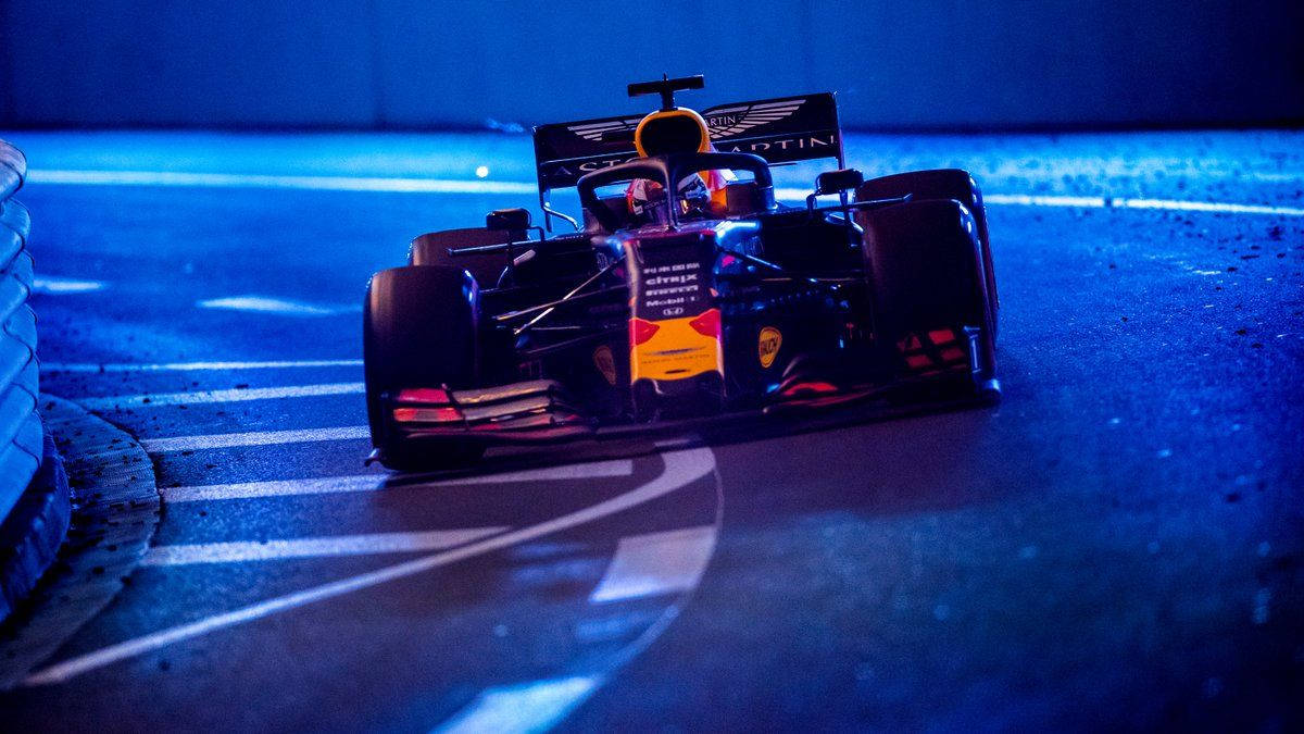 Verstappen 桌布 壁紙 — 一輛紅牛一級方程式賽車在霓虹藍色照亮的夜間賽道上滑行，帶有銳利的白色路緣和發光的倒影。