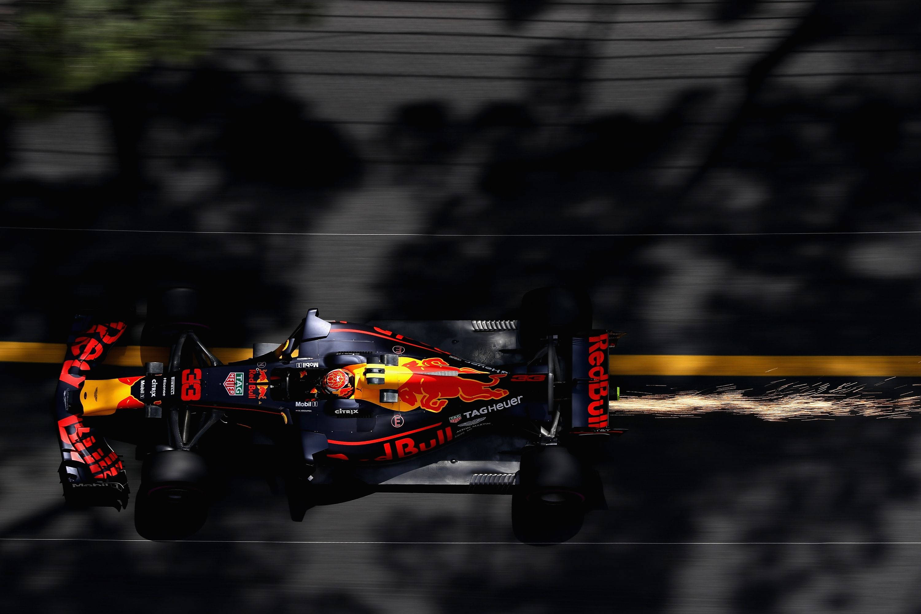 Verstappen 桌布 壁紙 — 一輛紅牛一級方程式賽車高速駛過，輪胎火花四濺，背景是模糊的黑暗賽道，兩旁樹木林立。
