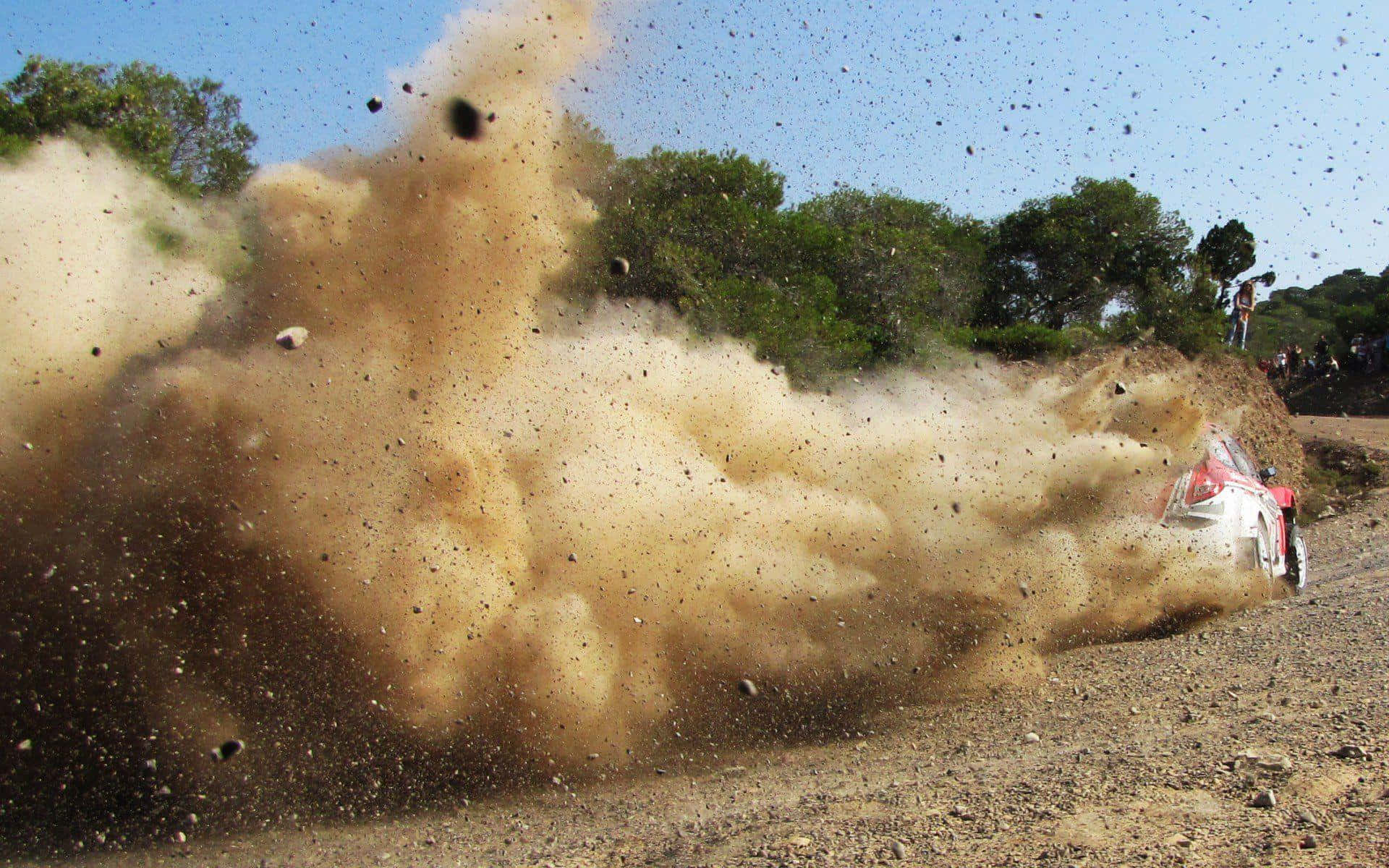 Dust 桌布 壁紙 — 一輛紅白相間的拉力賽車在碎石路上揚起巨大的棕色塵埃，背景有綠樹和觀眾。