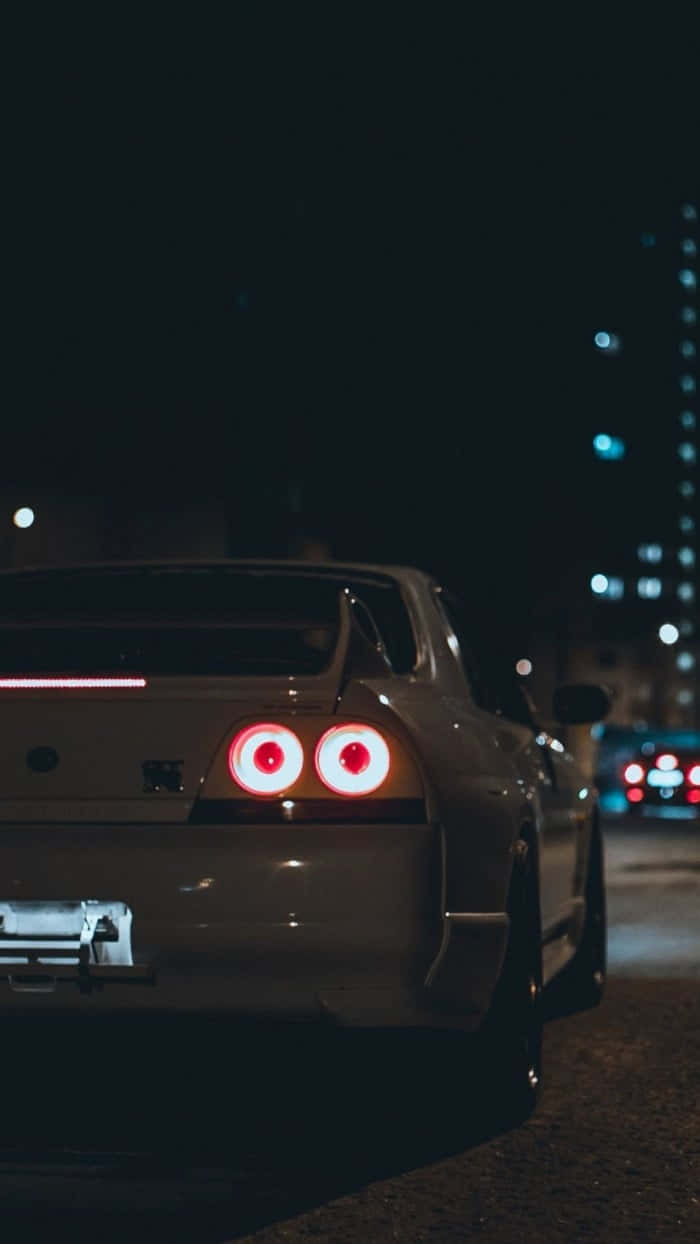 銀色跑車在夜晚的城市街道上，紅色尾燈發光。