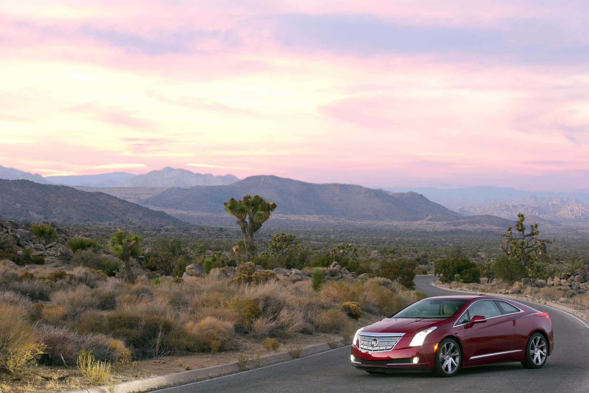 Cadillac Elr 桌布 壁紙 — 一輛紅色Cadillac雙門跑車在日落時分沿沙漠公路行駛，約書亞樹和遠山在粉紅和紫色的天空下。