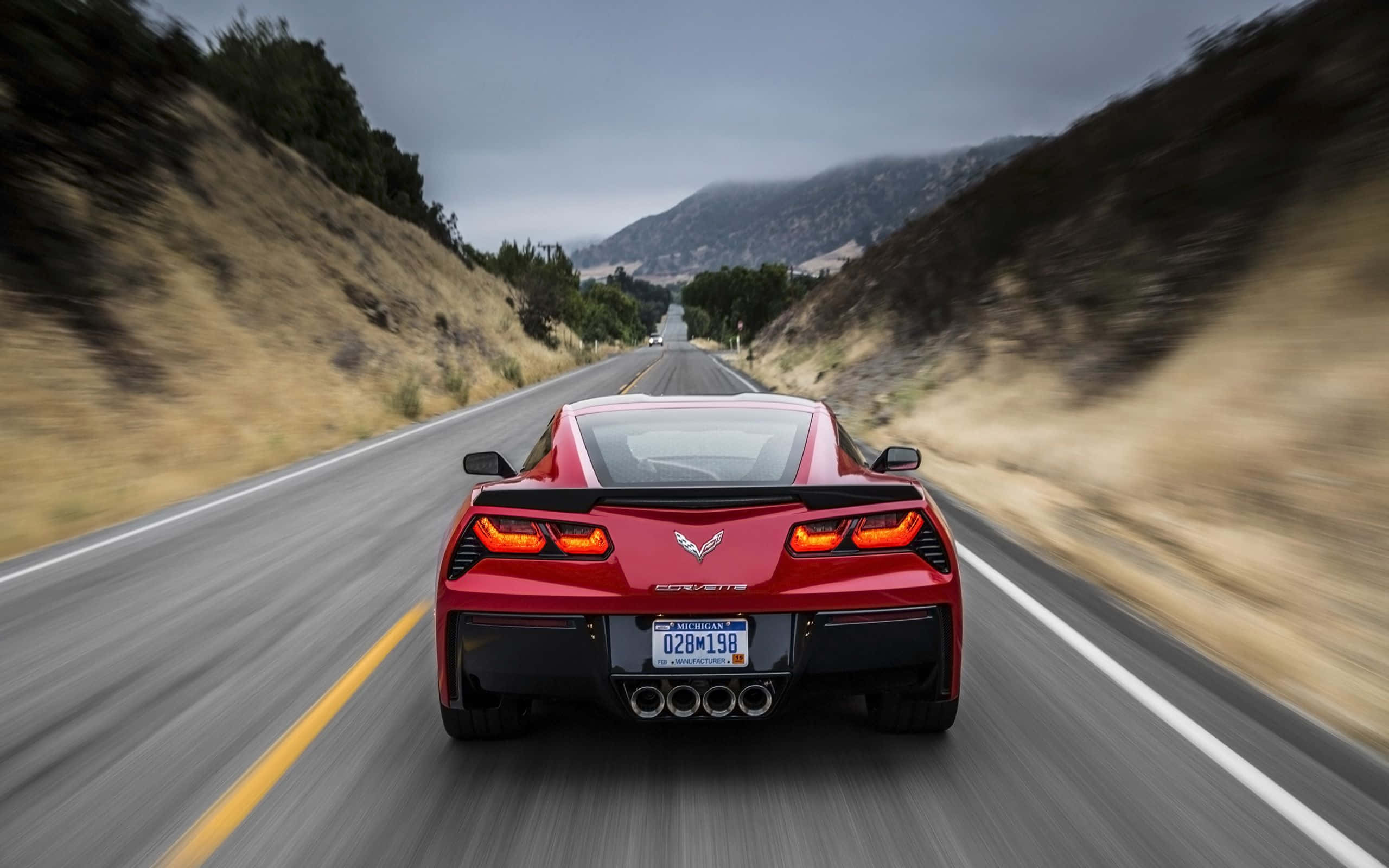 corvette 桌布 壁紙 — 一輛紅色Corvette跑車在蜿蜒的山路上飛馳，周圍環境模糊，天空多雲。