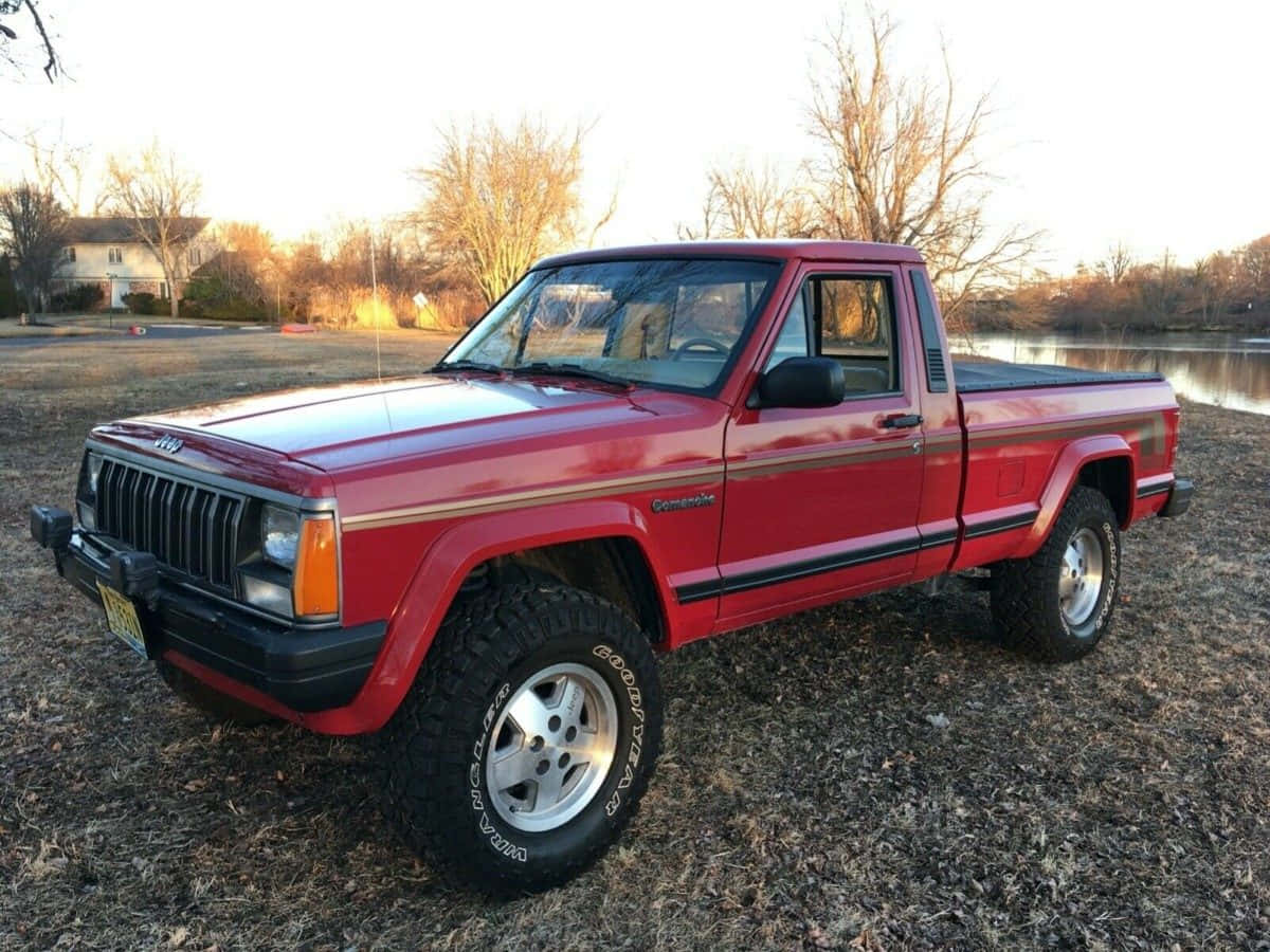 Jeep Comanche 桌布 壁紙 — 一輛紅色Jeep Comanche皮卡車配備大型輪胎，停在日落時分湖邊的乾草上。