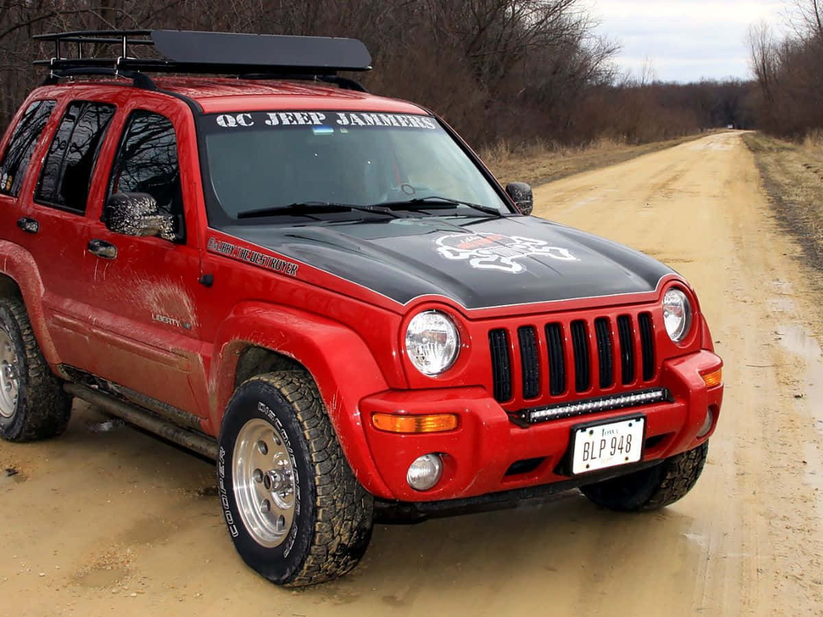 Jeep Liberty 桌布 壁紙 — 一輛紅色Jeep Liberty，黑色引擎蓋和車頂行李架，停泊在泥濘的土路上，周圍是光禿禿的樹木。