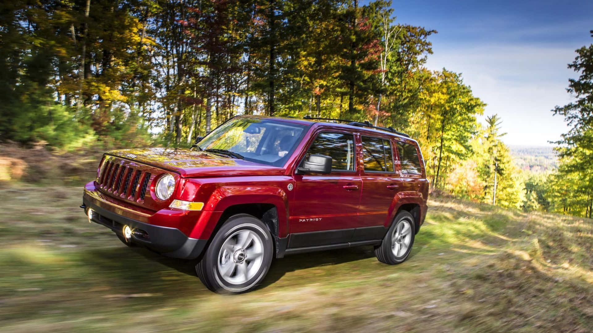 Jeep Patriot 桌布 壁紙 — 一輛紅色Jeep Patriot在晴朗藍天下駛過秋葉林間。