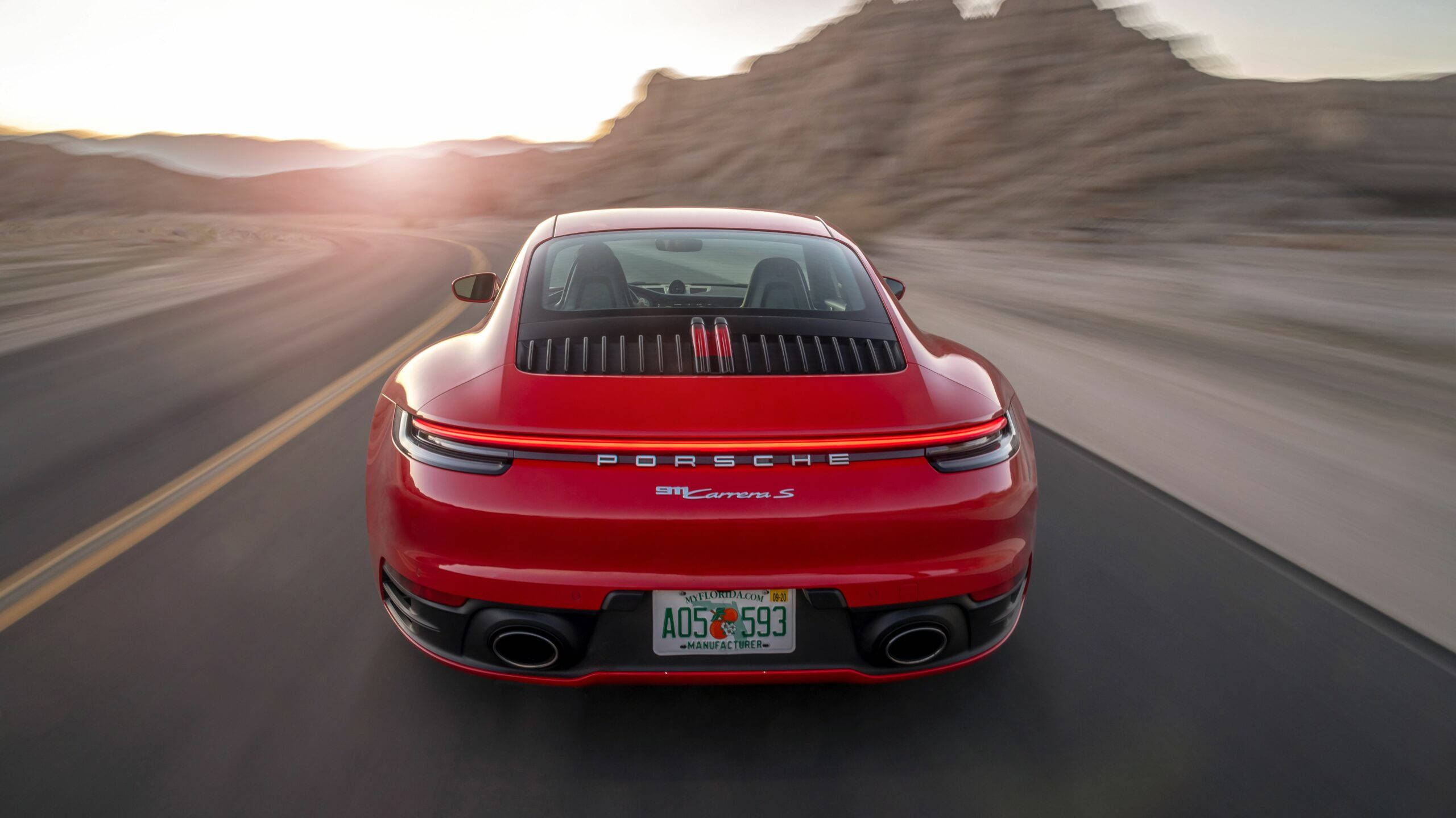 保時捷 桌布 壁紙 — 一輛紅色保時捷911 Carrera S在日落時分在沙漠公路上高速行駛，路面呈現動態模糊效果。