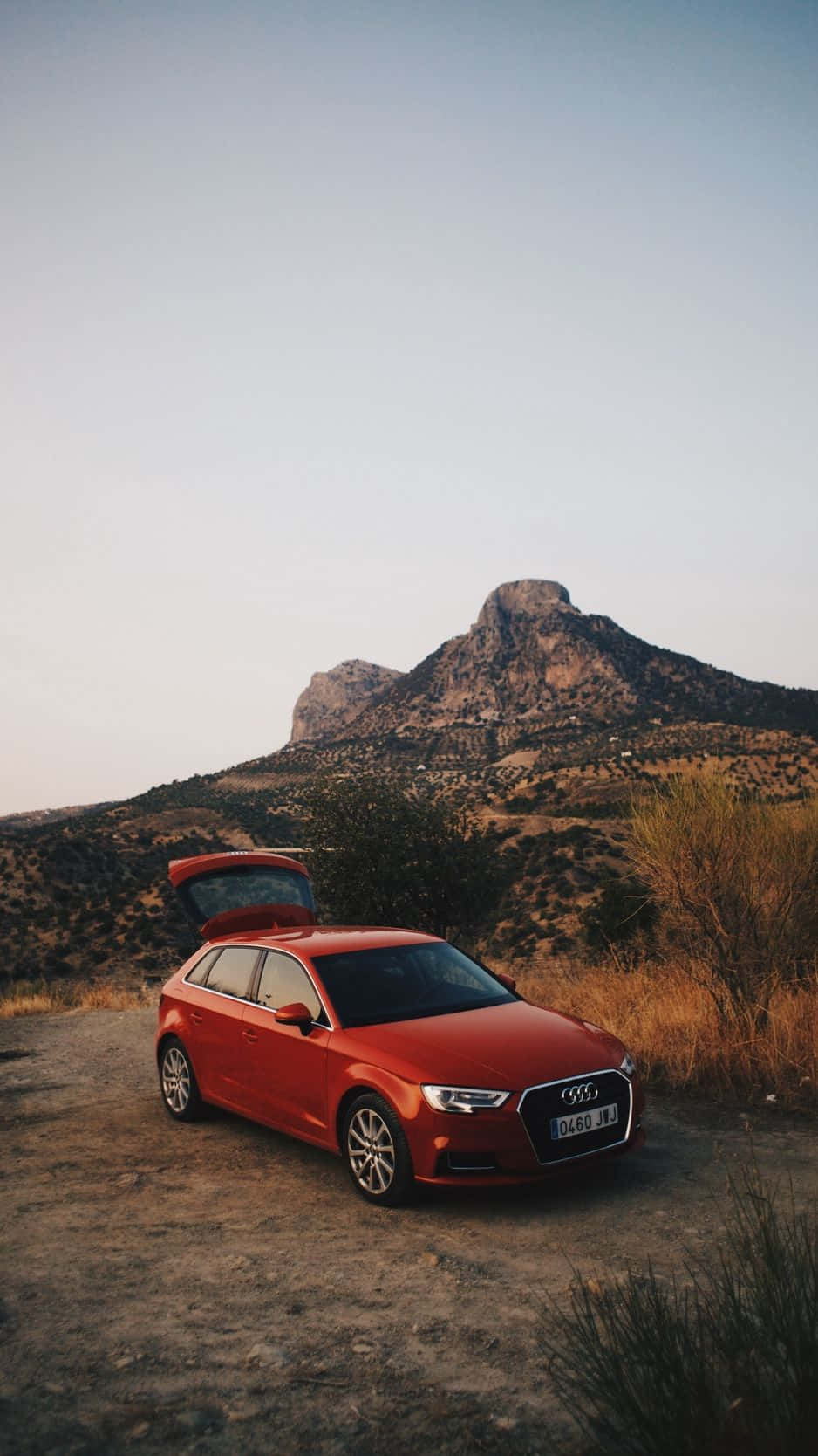 Audi Q5 桌布 壁紙 — 一輛紅色奧迪旅行車停在泥路上，尾門打開，背景是崎嶇的沙漠山脈，正值黃金時刻。